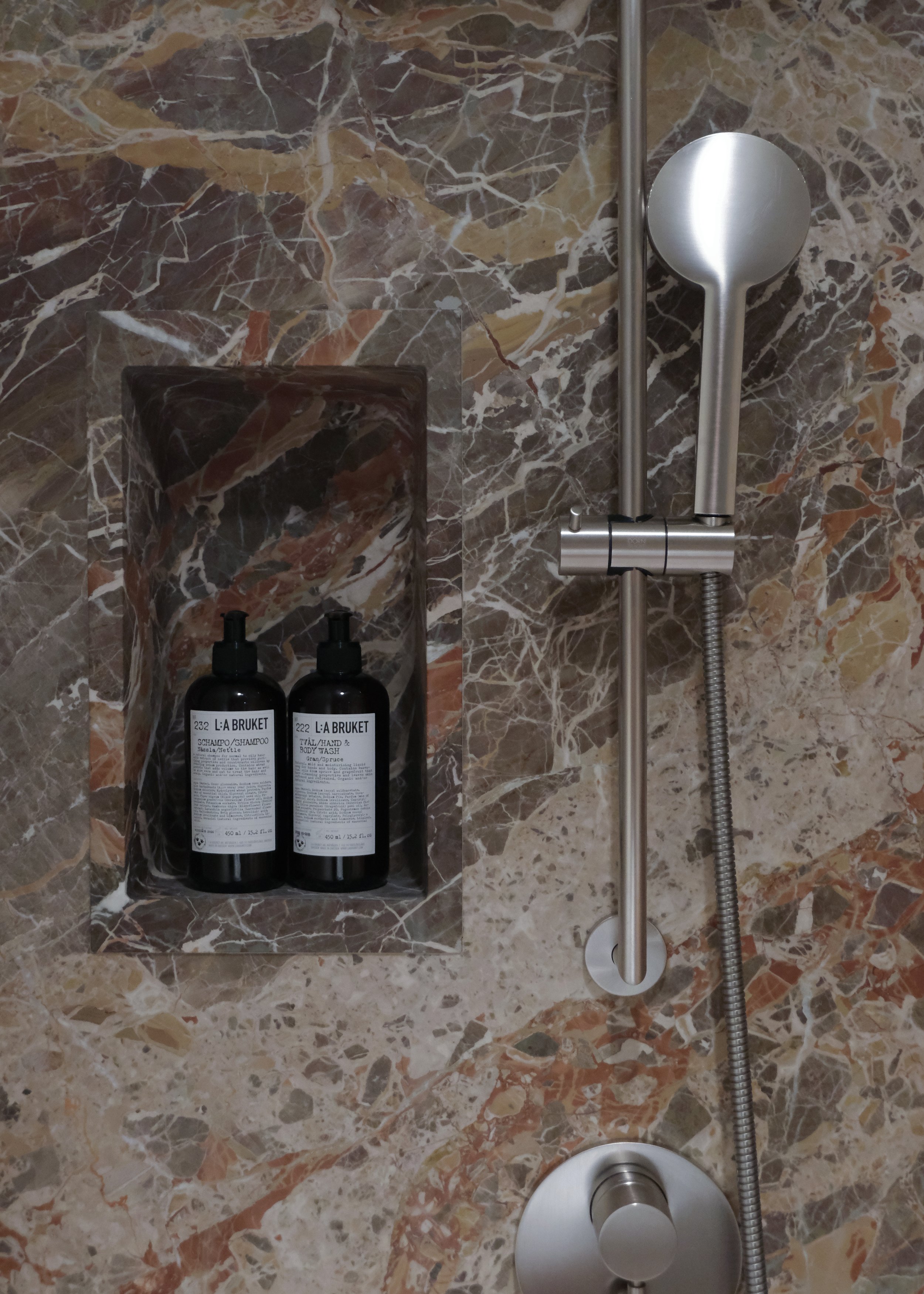 Duschbereich mit Armatur, Brausekopf, Seifenspendern, und Wandnische aus Marmor
