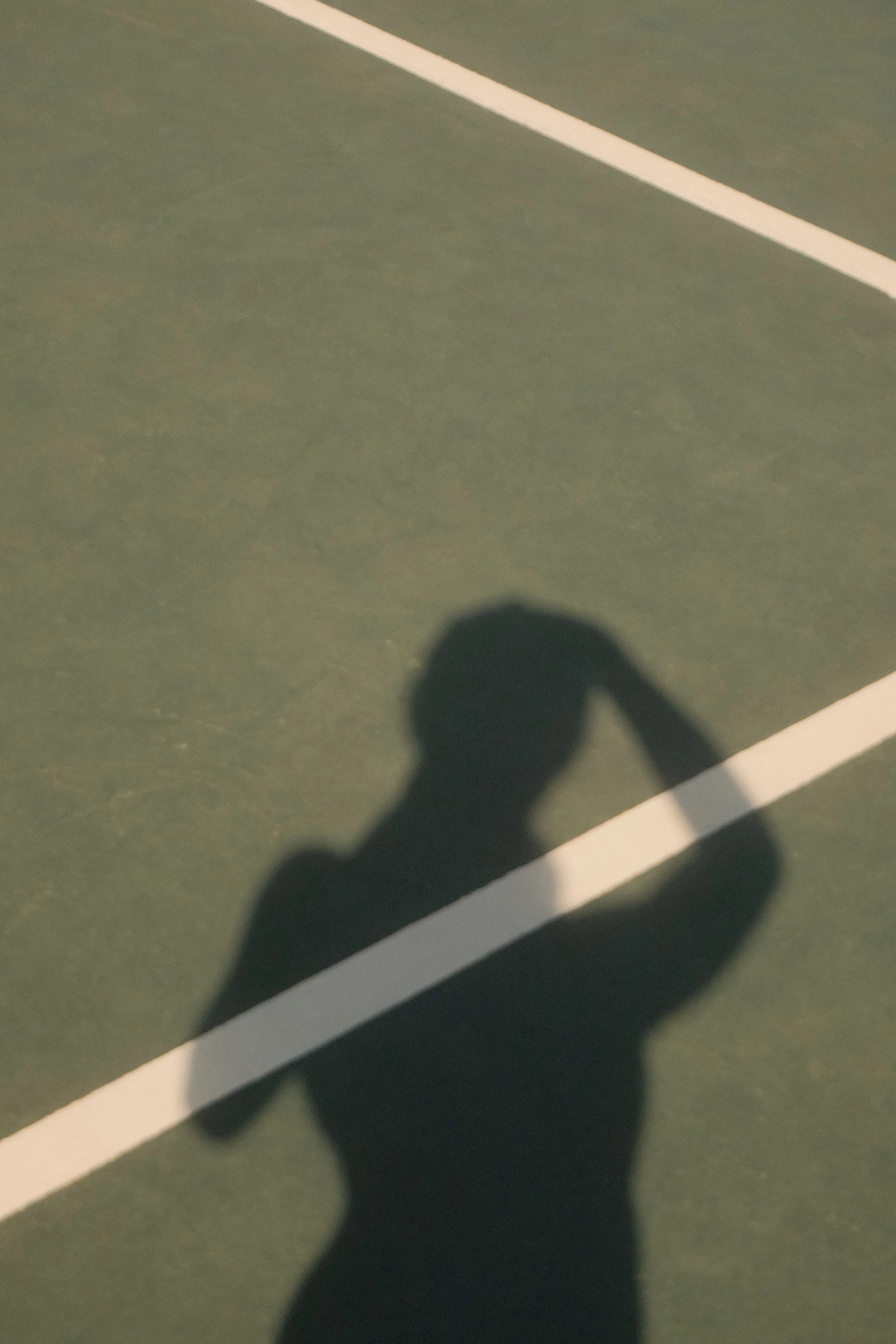 Schatten einer Person auf einem Tennisplatz bei Sonnenuntergang.