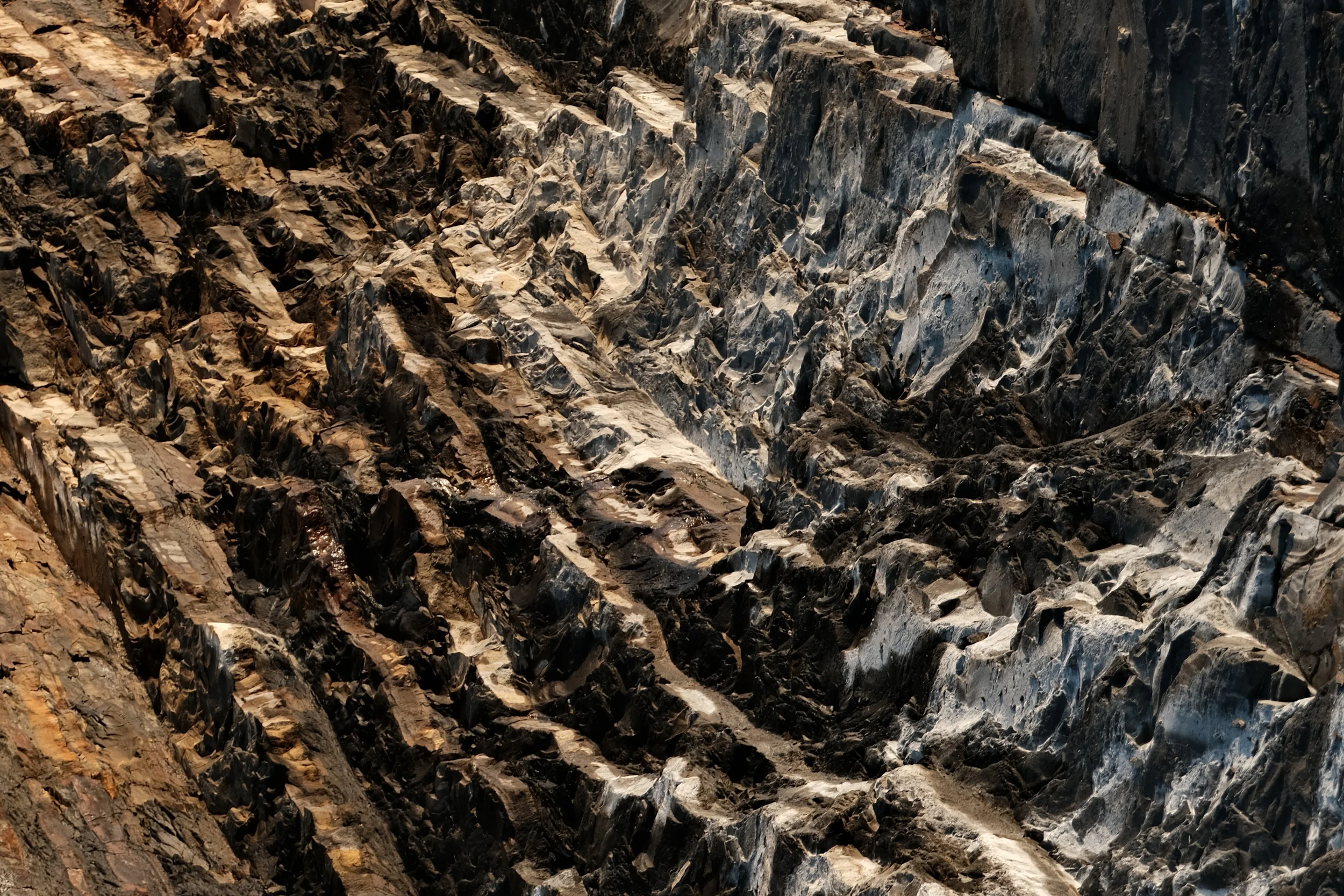 Nahaufnahme einer schieferbedeckten Wand mit unterschiedlich gefärbten Schieferschichten in Schwarz, Grau und Braun.