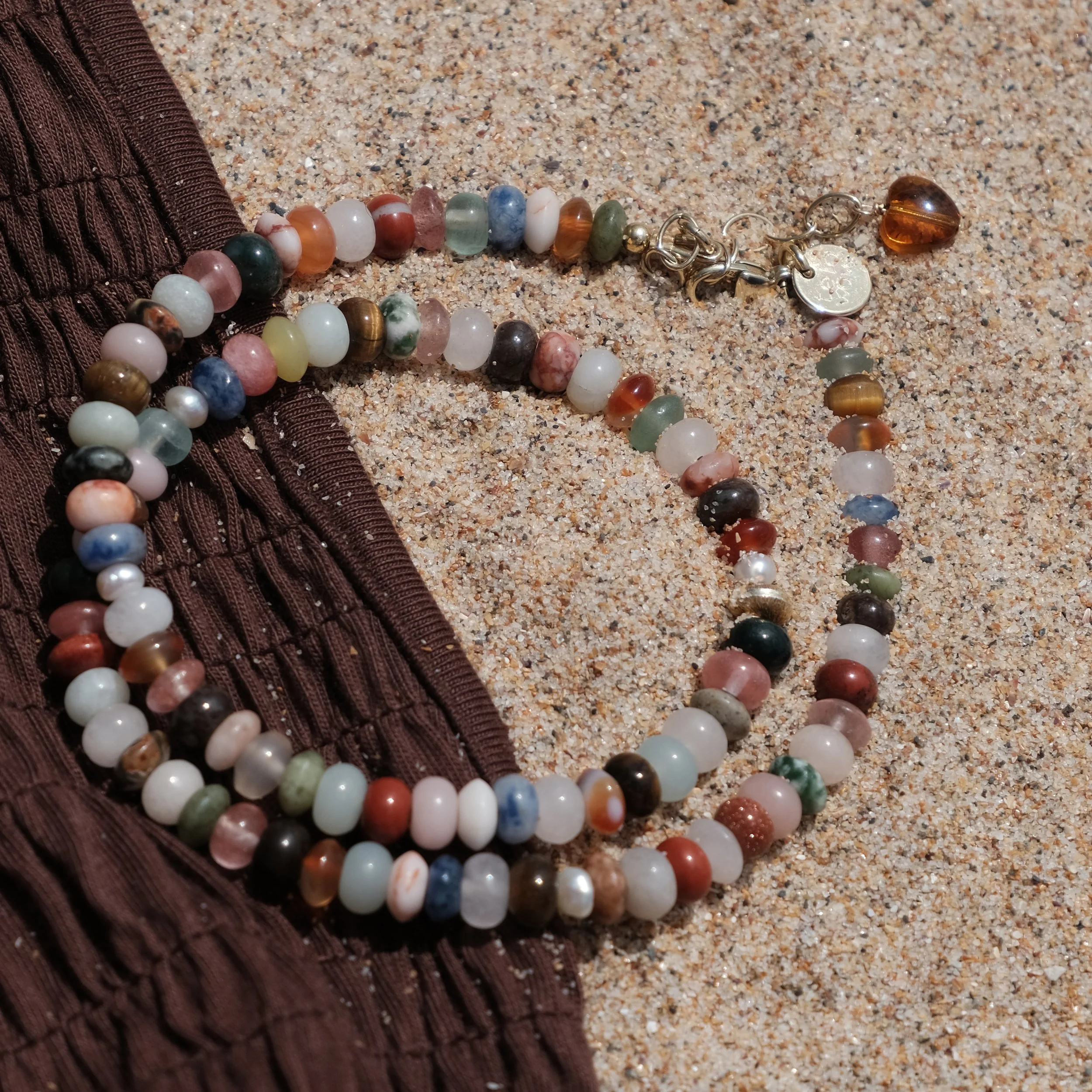 Perlenkette auf Sand mit braunem Textilstoff.