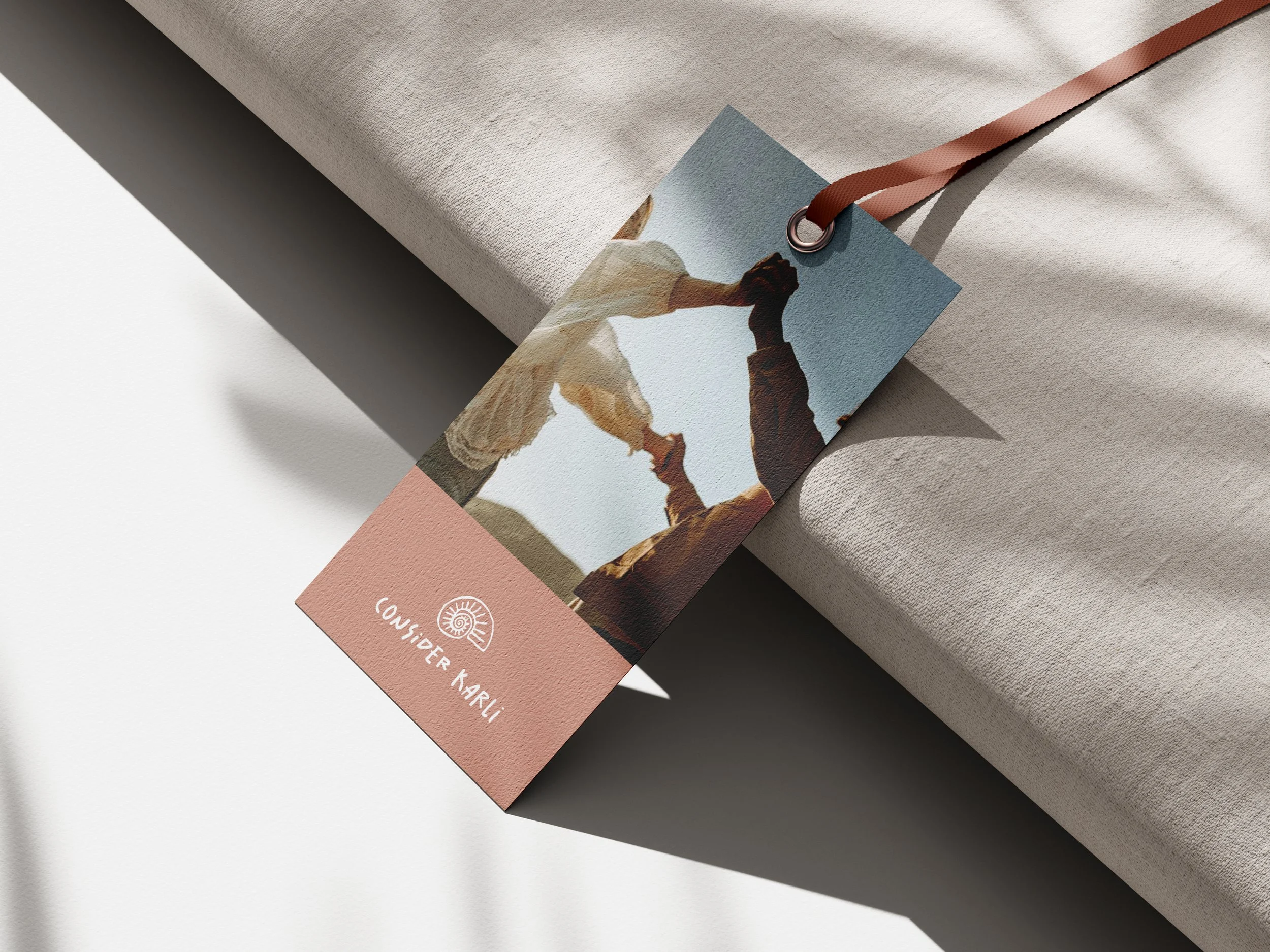 Werbeetikett mit dem Schriftzug "CONSIDER KAHLi" und einem Bild von zwei Menschen, die Hände halten. Das Etikett ist an einem Stoff befestigt. Licht- und Schatteneffekte sind sichtbar.