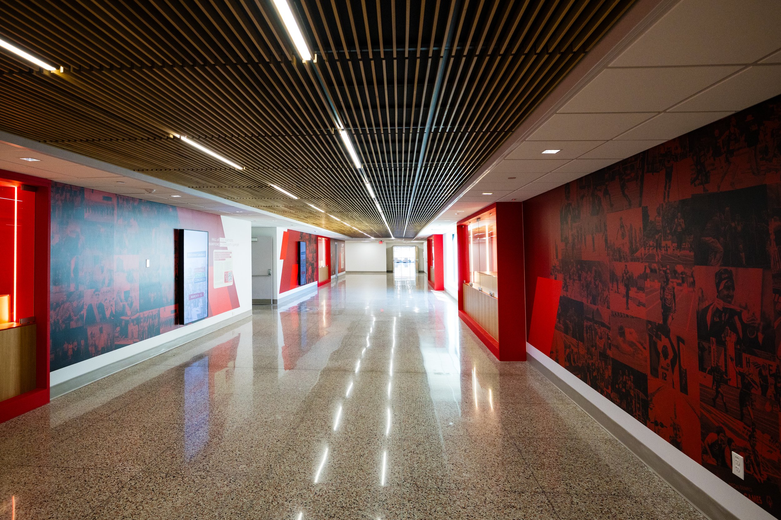 Empty hallway with red and black murals on the walls, polished floors, and a wooden slatted ceiling with embedded lighting.
