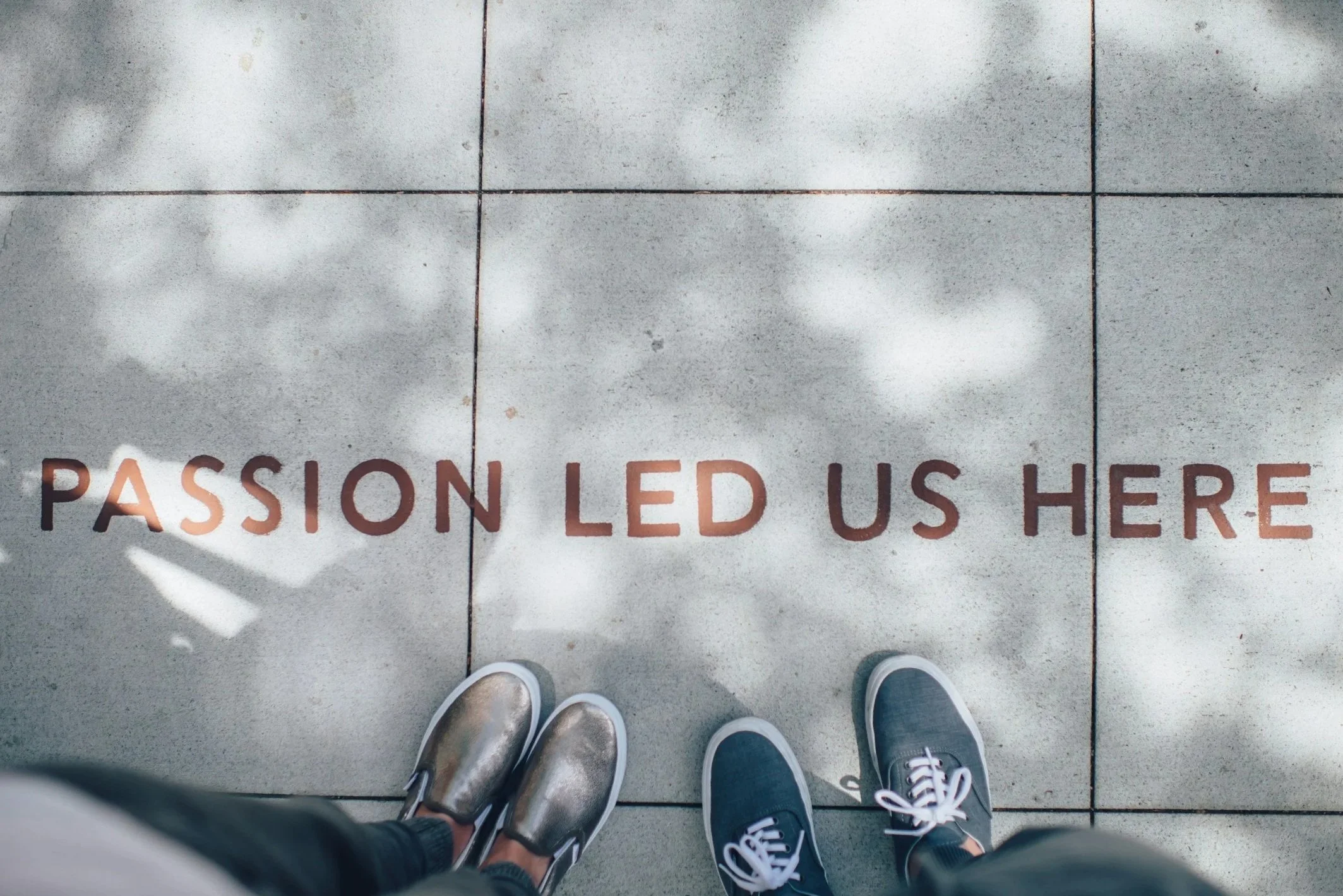 View of two pairs of shoes standing on a tiled floor, with a motivational message on the floor that says "PASSION LED US HERE."