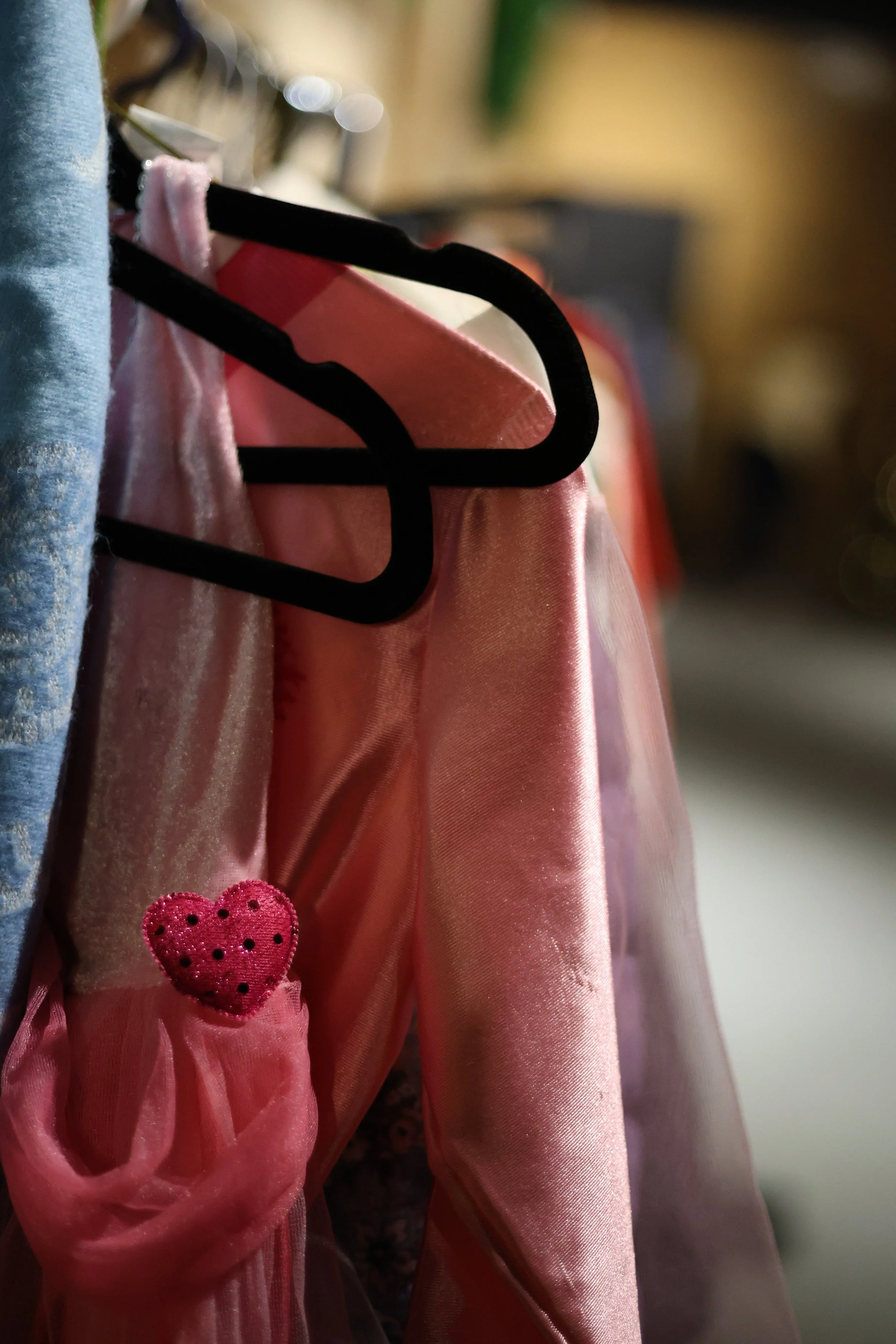 Close-up of pink dresses hanging on black hangers, featuring a small heart-shaped embellishment with black polka dots.