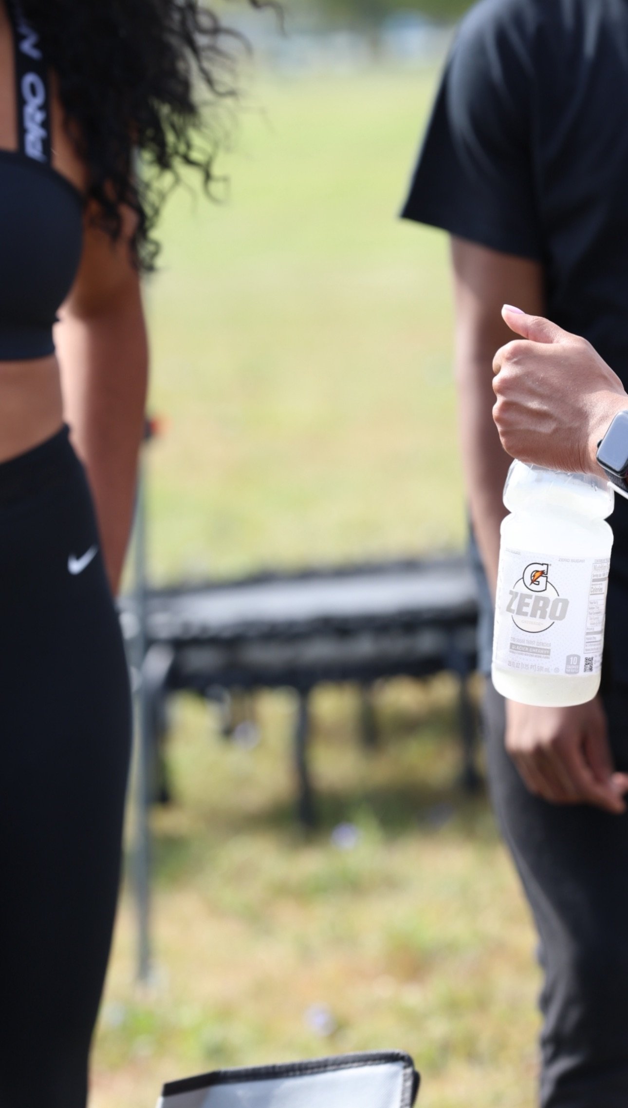 Close-up of two people, one holding a Gatorade drink, the other with a smartwatch, at an outdoor event.