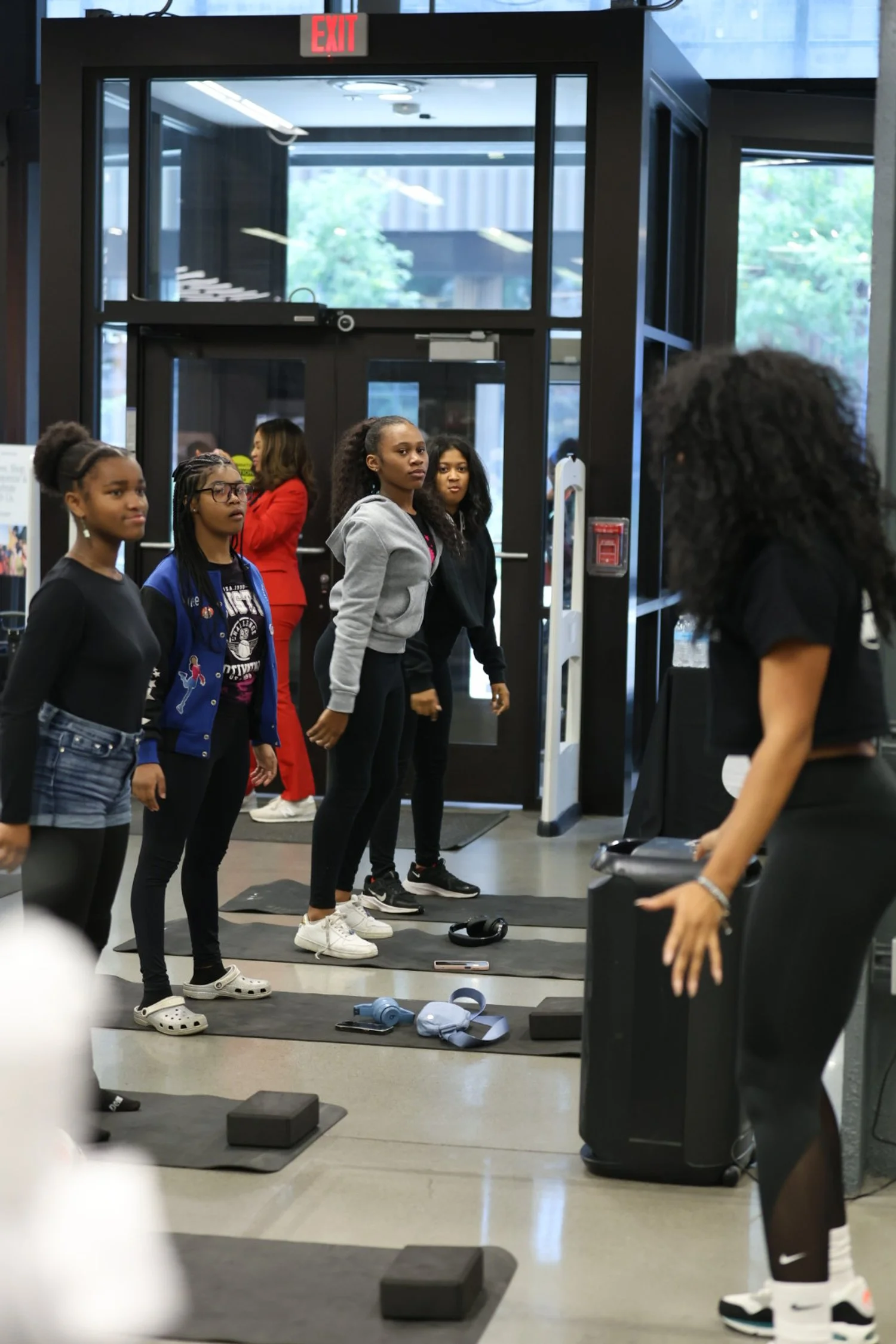 Group of young women participating in a fitness class at a gym, standing on exercise mats in front of an instructor.