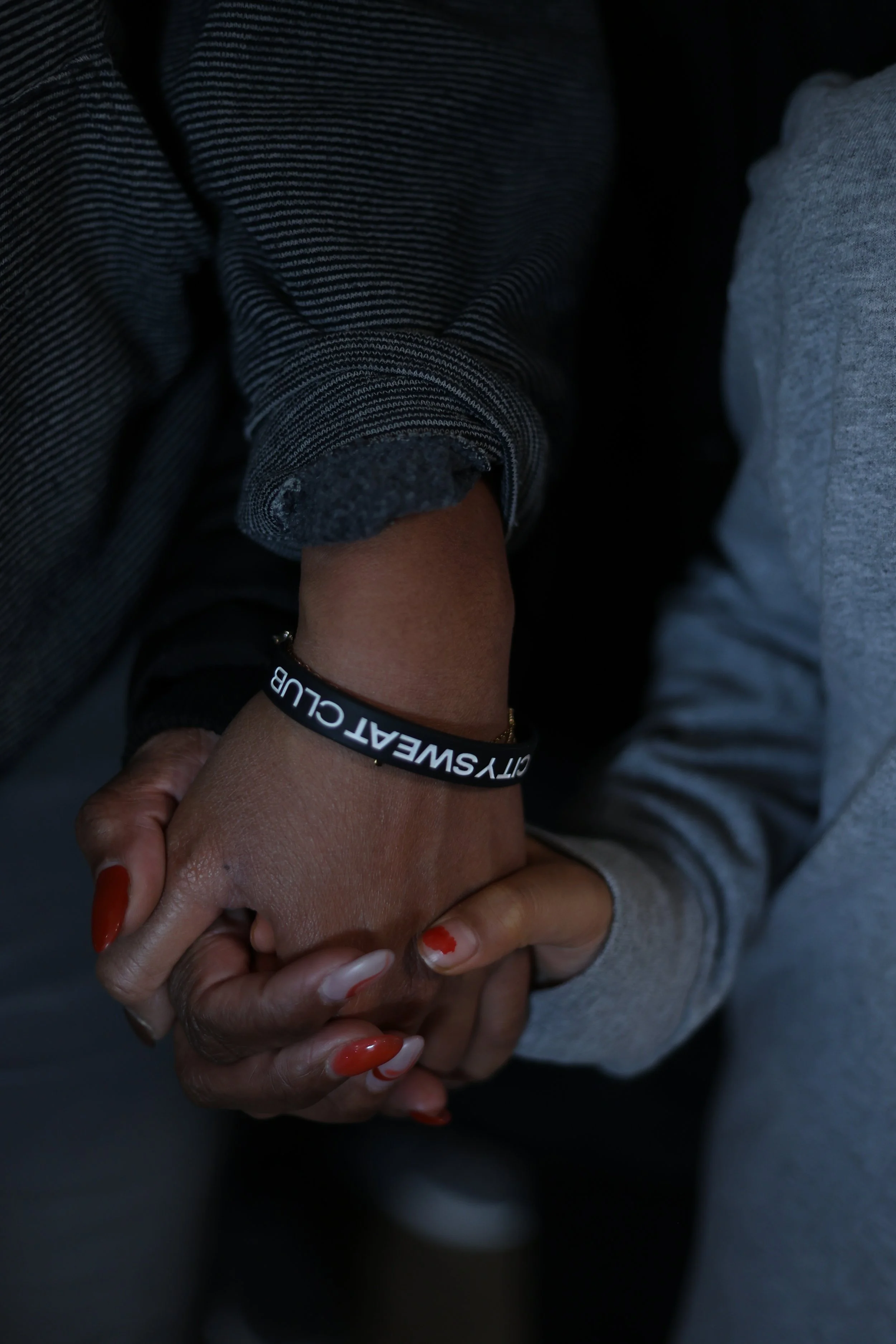 Two people holding hands, one wearing a black silicone bracelet with white text, the other with red and white painted nails.