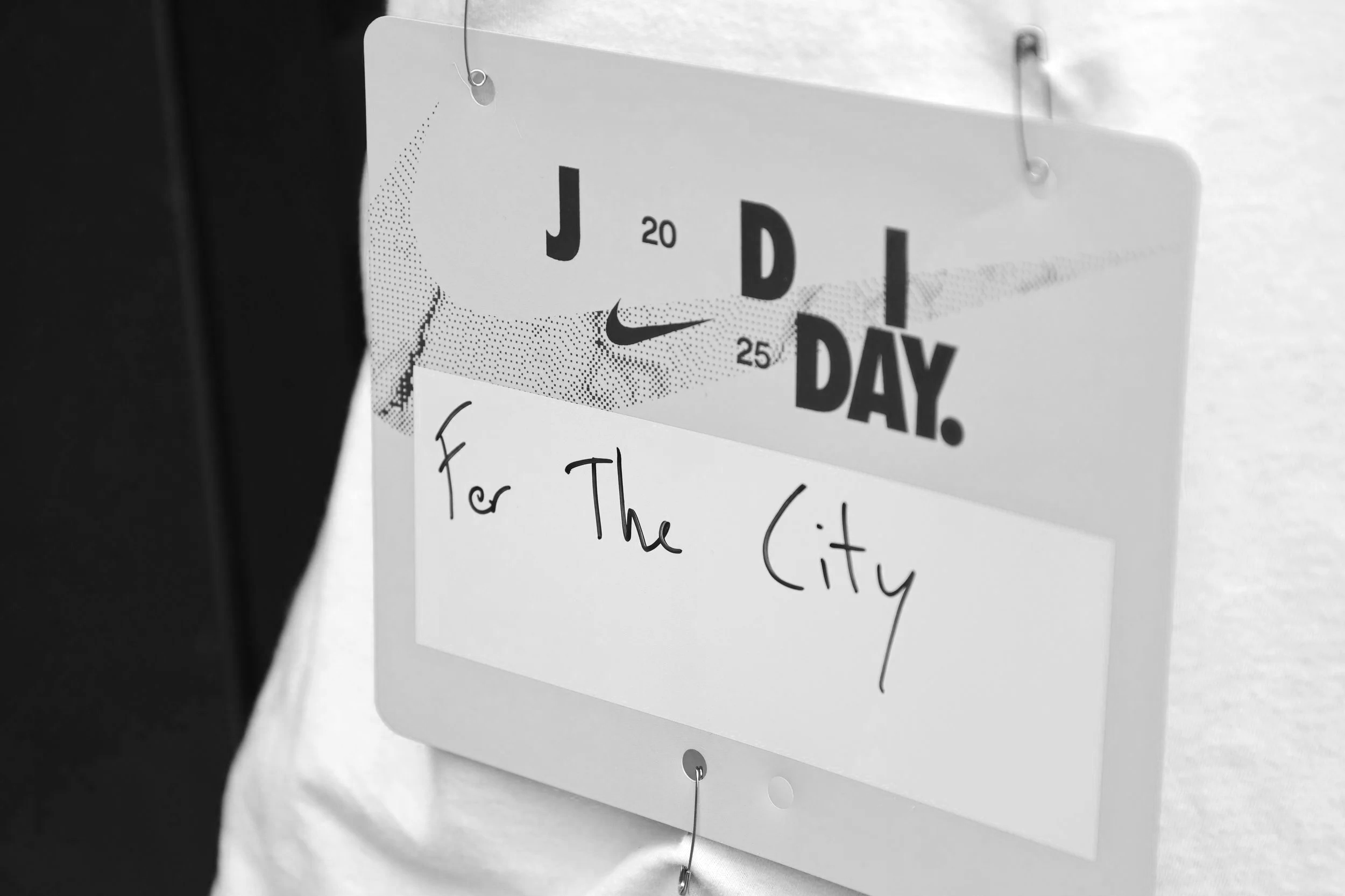 A sign hanging on a wall with the text 'J 20 25 D I DAY.' and handwritten note that says 'For The City'.