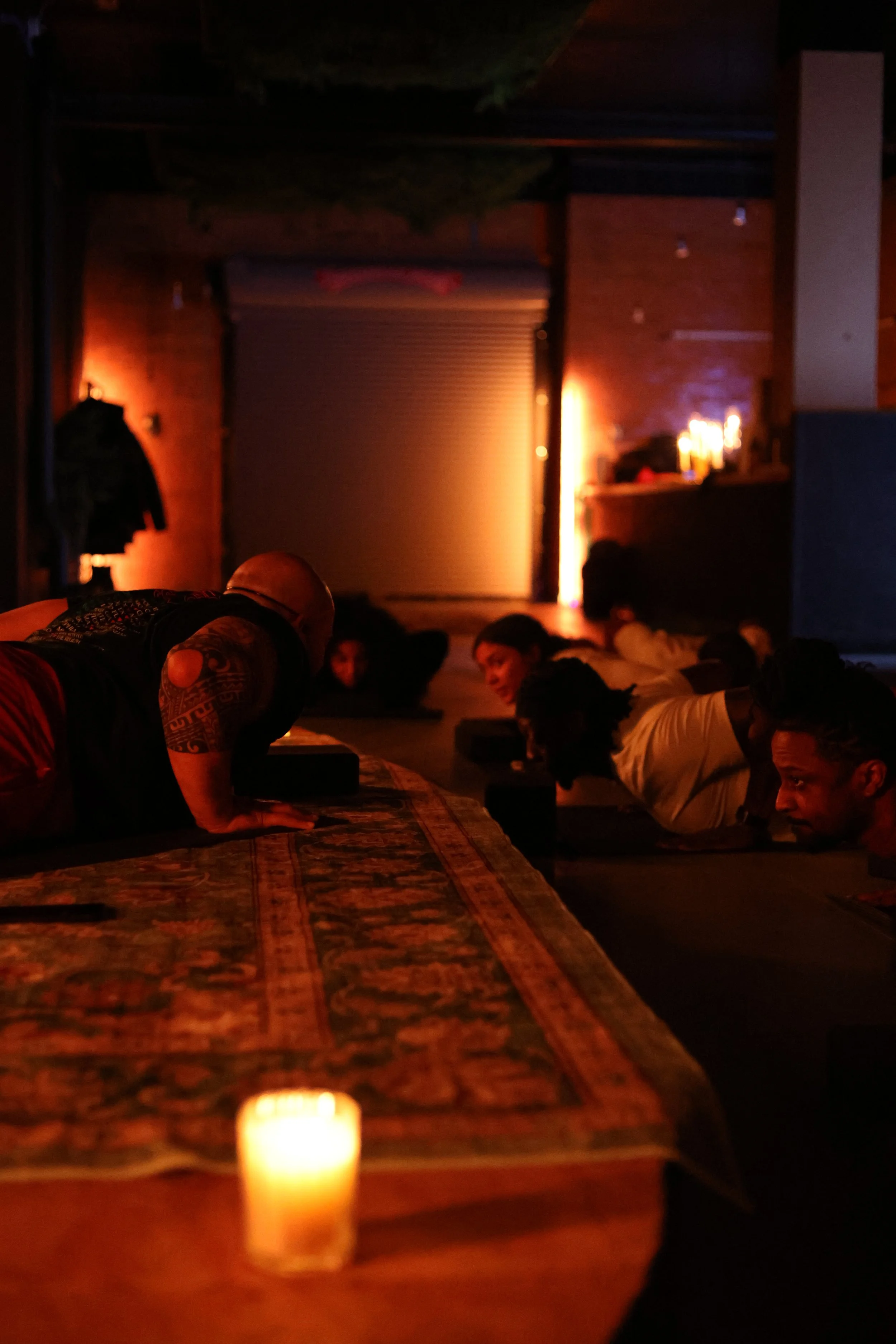 People doing yoga or meditation in a dimly lit room with a mysterious ambiance, illuminated by candles and soft lighting.