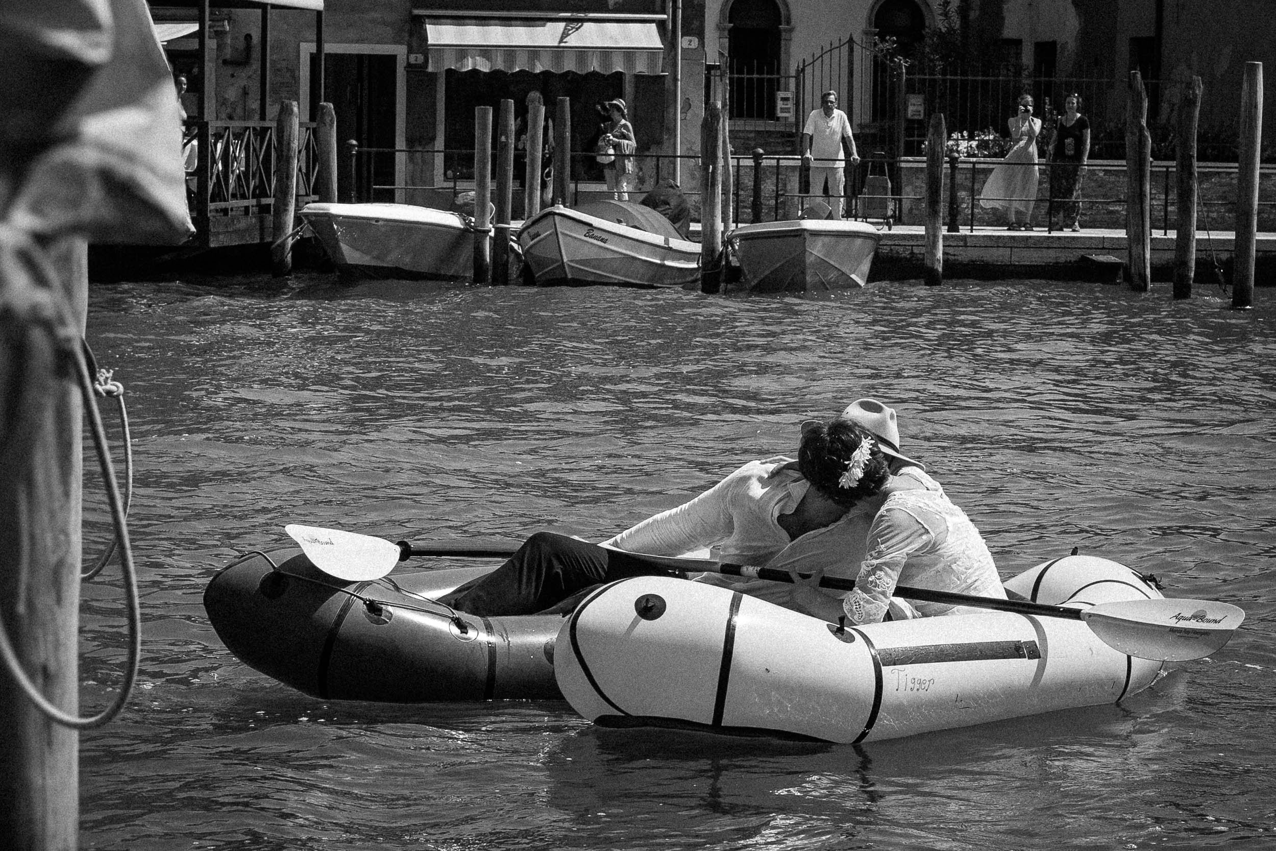 Black and white photo of bride and groom kissing while they canoes touch on a Venice canal in Italy.