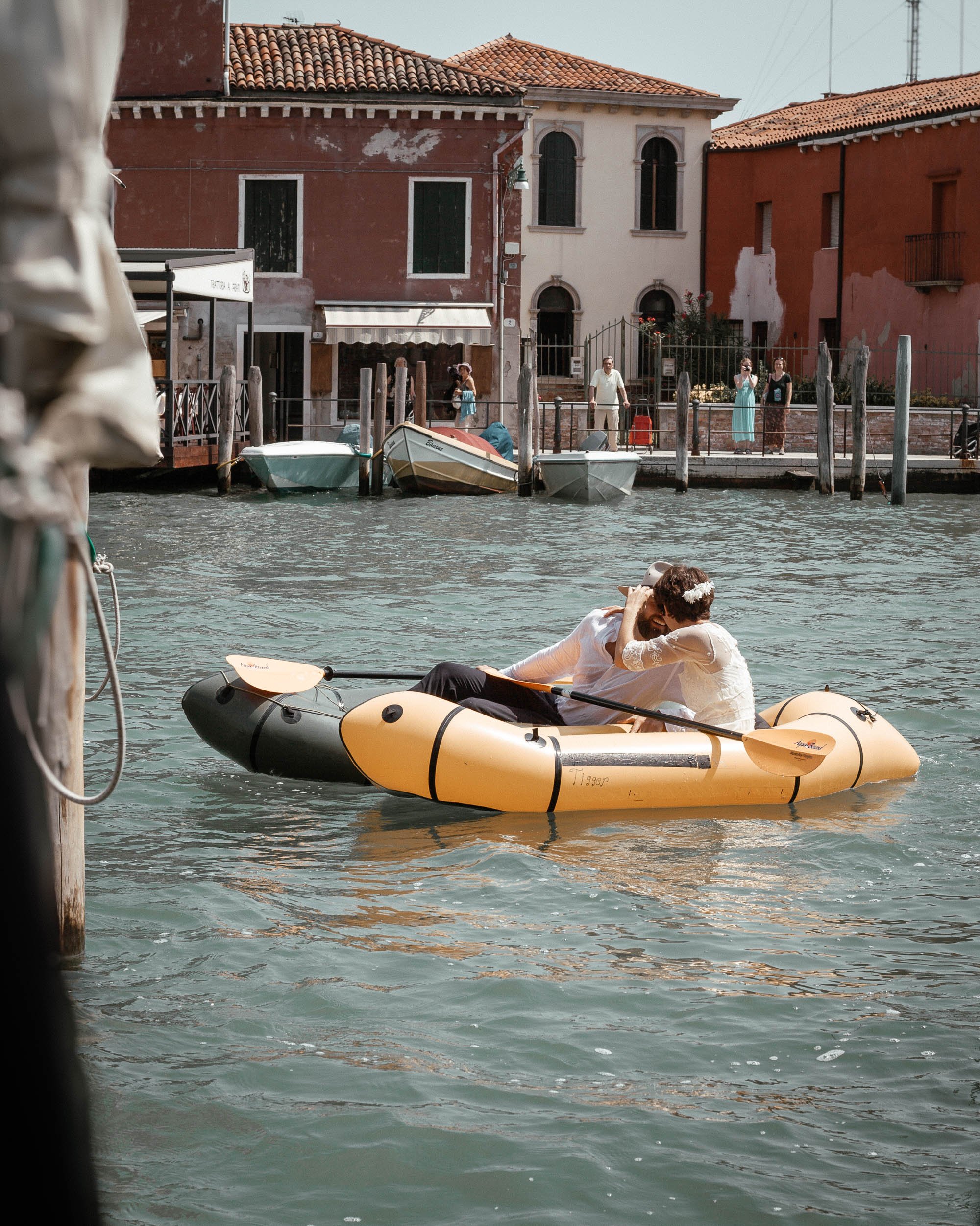Bride and groom kiss while riding canoes in Venice under the eyes of onlookers.