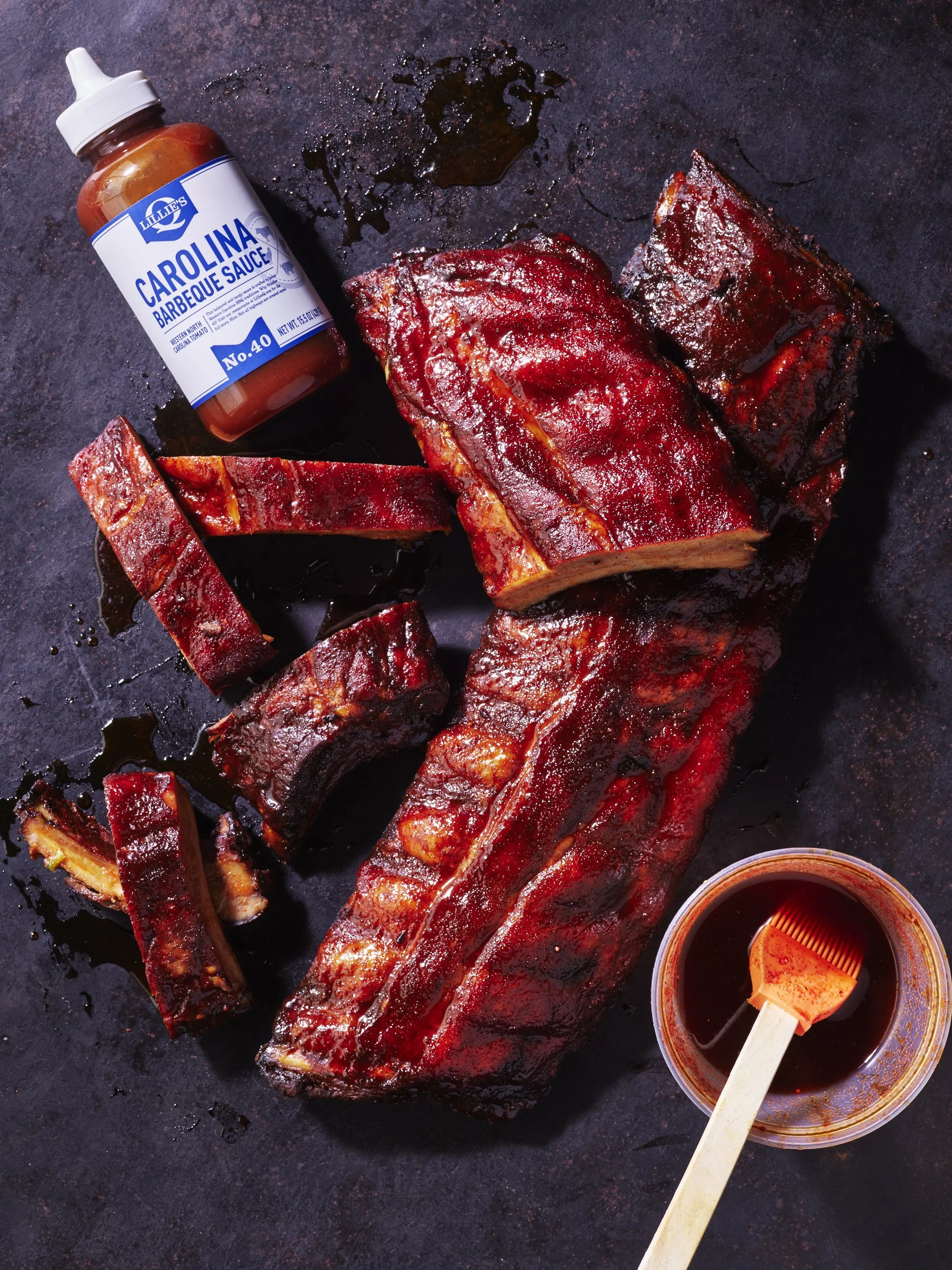 Raw red meat and food products arranged on a dark surface with rustic styling for a food brand editorial shoot