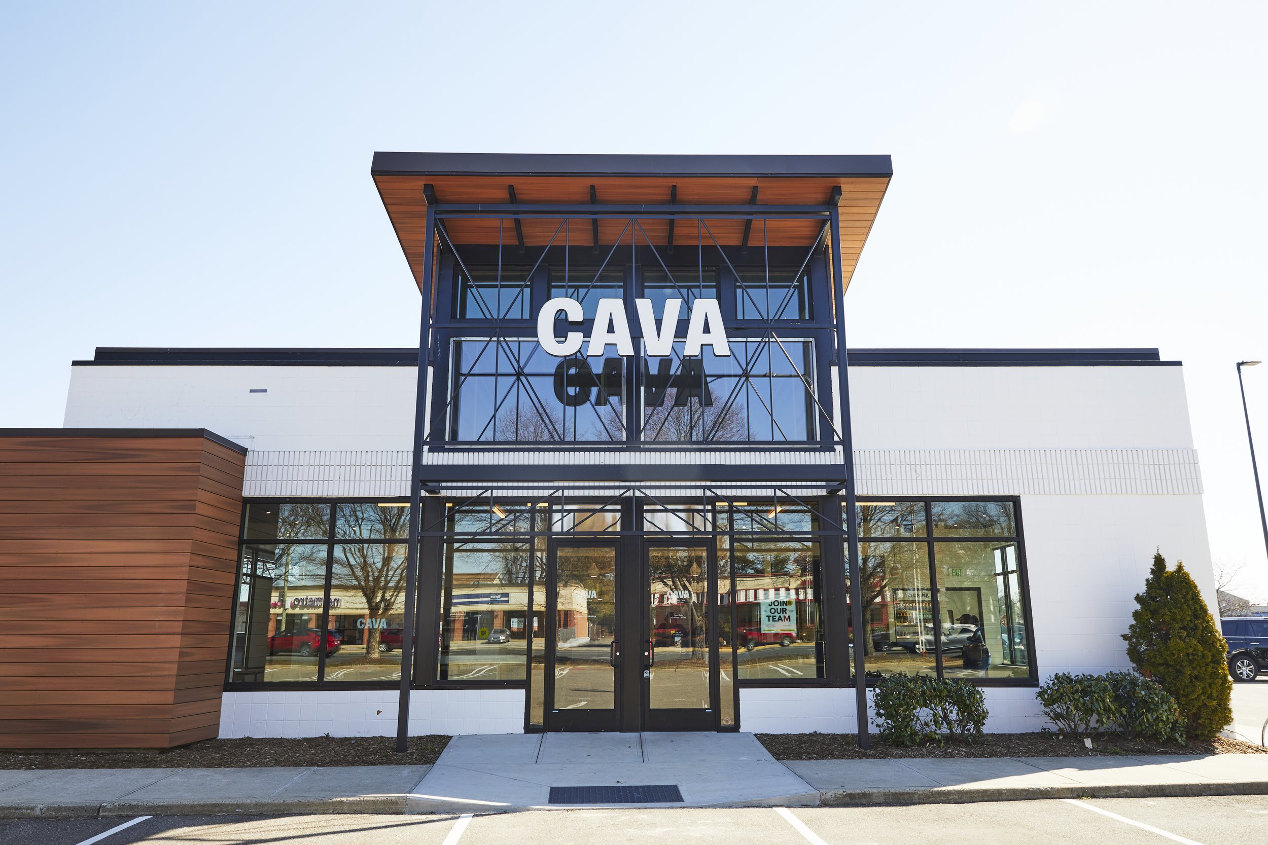 Exterior of a modern CAVA restaurant location with bold signage and large glass windows on a bright sunny day