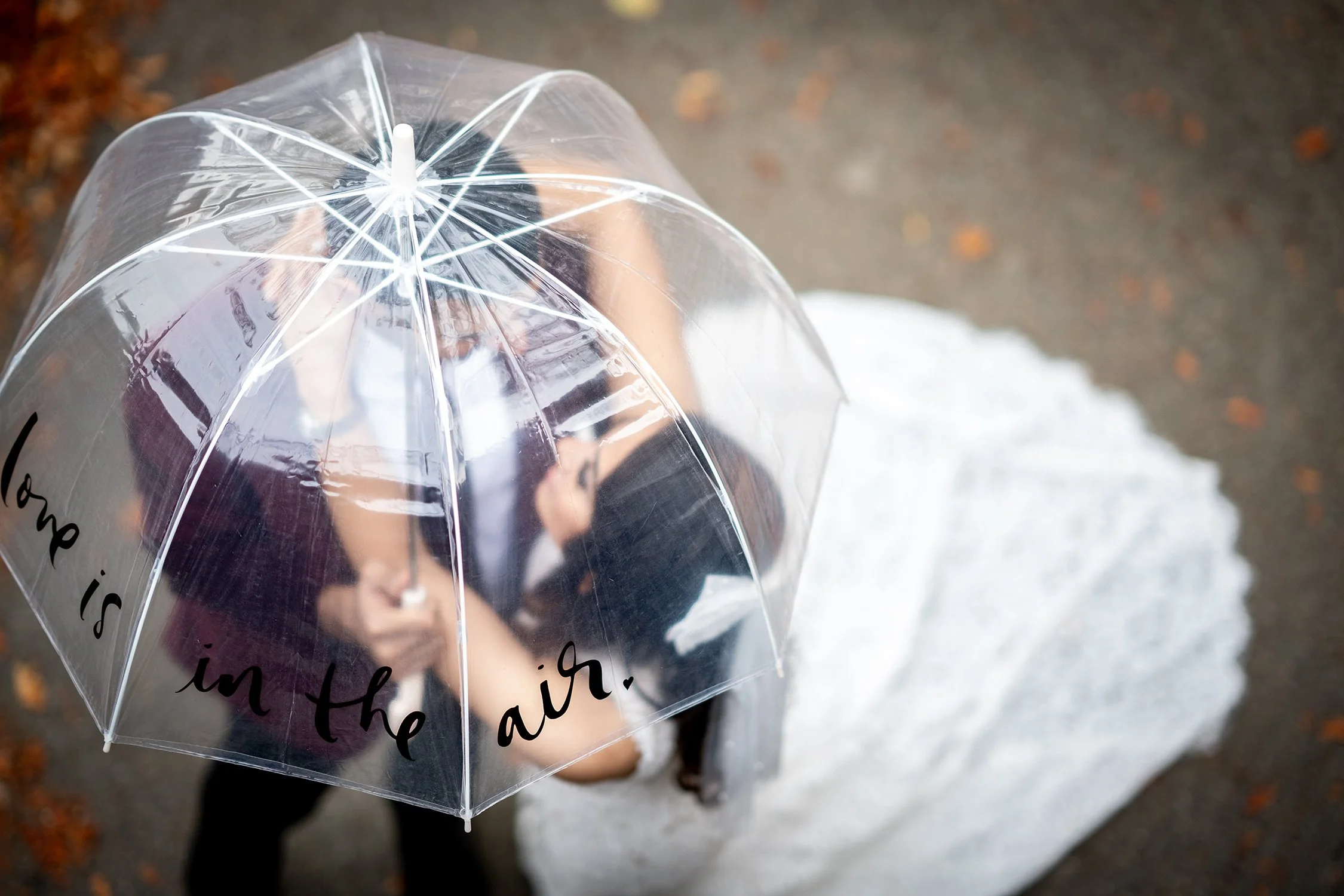 A bride in a wedding dress holding a transparent umbrella with the words 'Love is in the air' written on it,zz