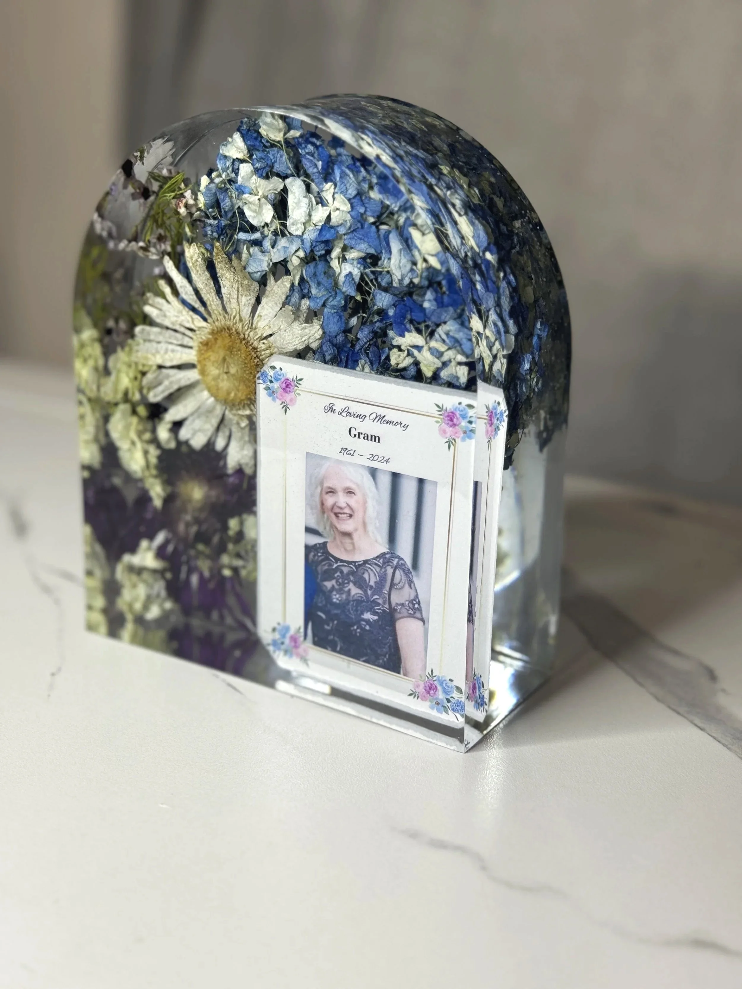 A memorial arch resin block with blue and white dried flowers inside.