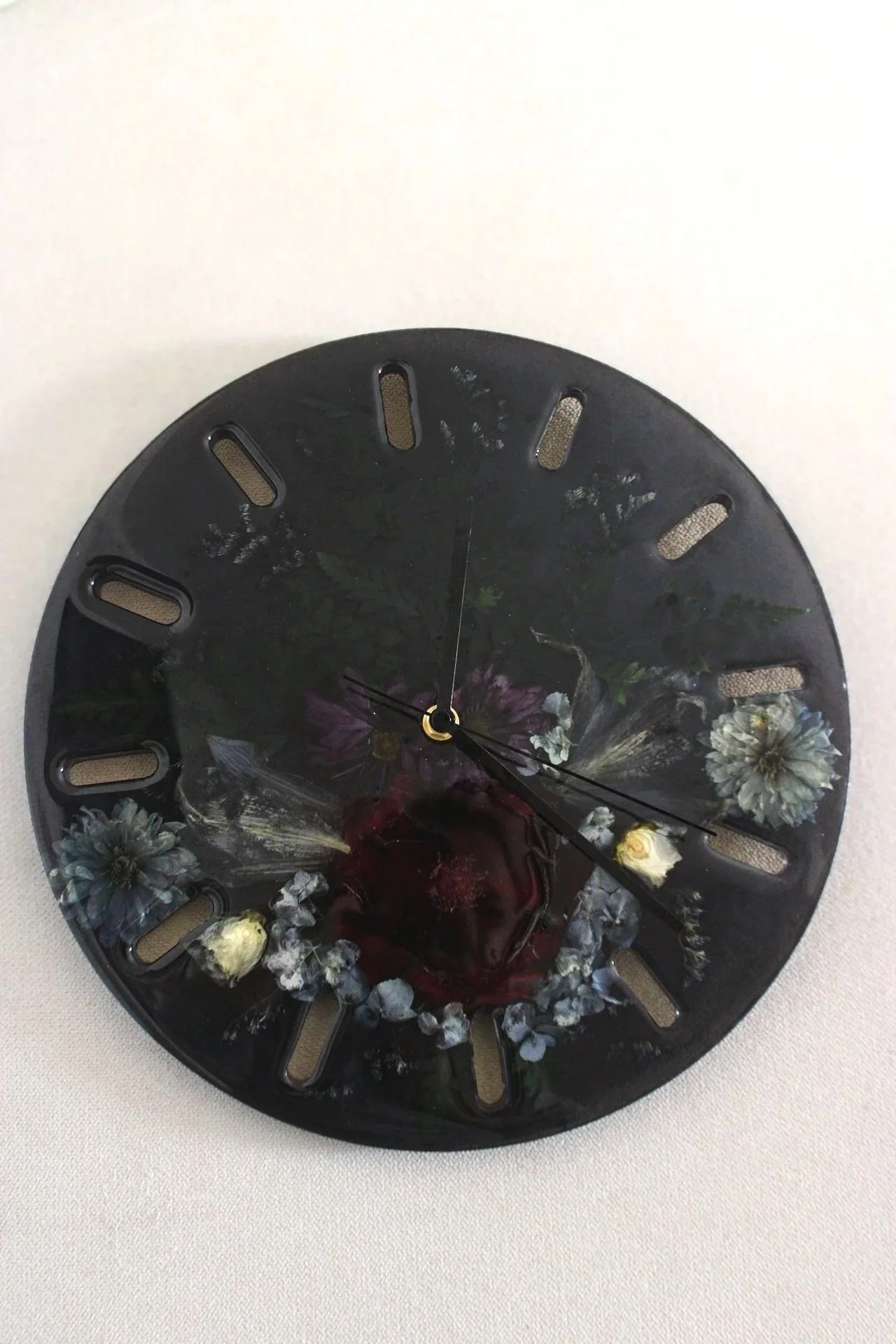 A wedding bout and flower preservation clock, featuring a dark background and various flowers, mounted on a plain light-colored wall.