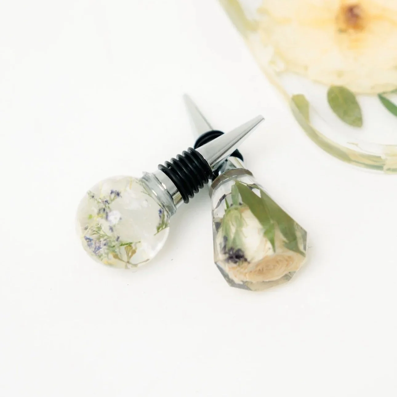 wine bottle stoppers containing dried flowers, lying on a white surface next to a glass container.