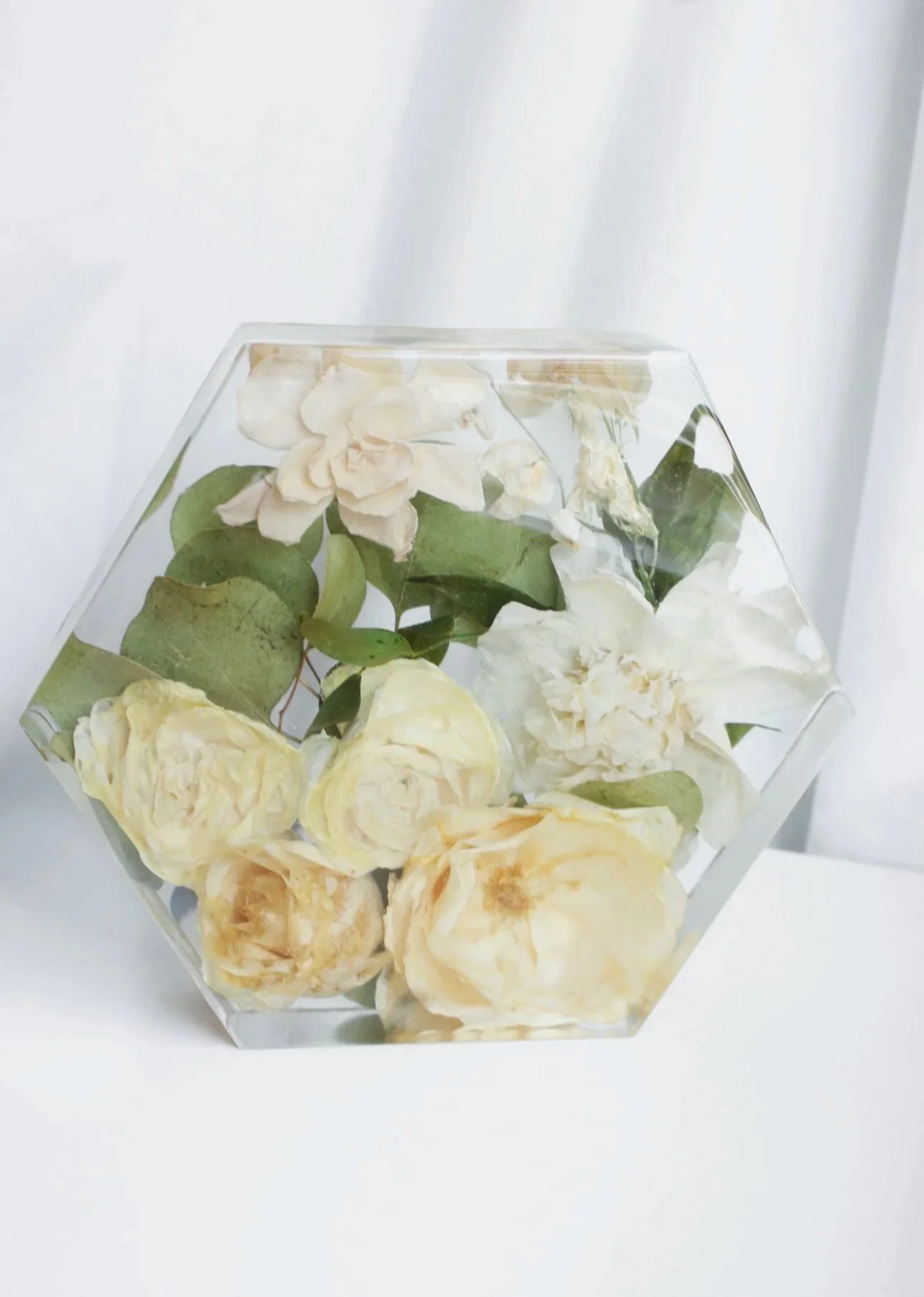 A flower preservation hexagonal container filled with dried white flowers and green leaves.