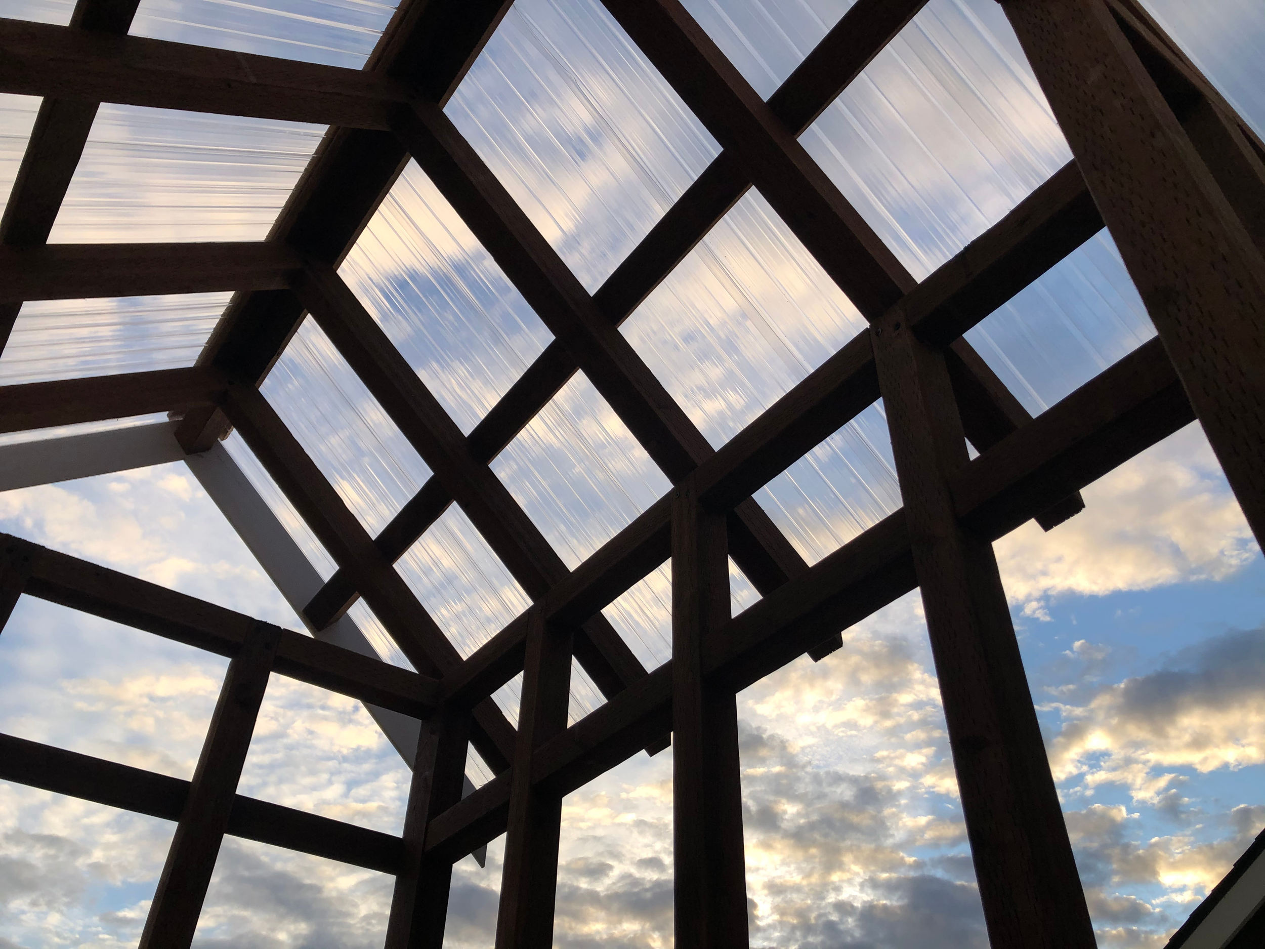 Photograph of the Igneous Greenhouse under construction. Open sky through the opening in a wooden construction frame, with clouds and patches of blue sky visible.