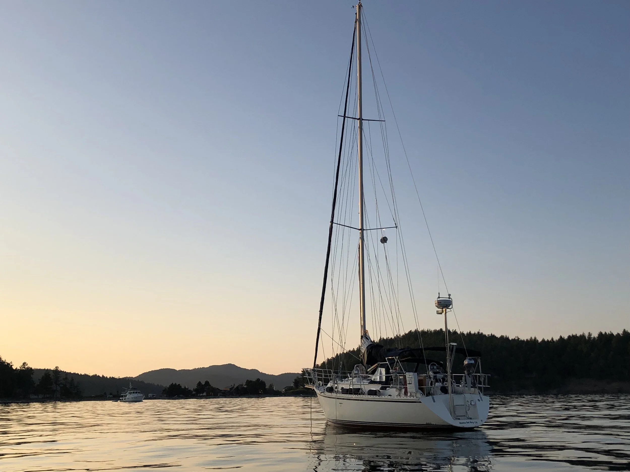 A sailboat docked on calm water during sunset, with a distant shoreline and mountains in the background.