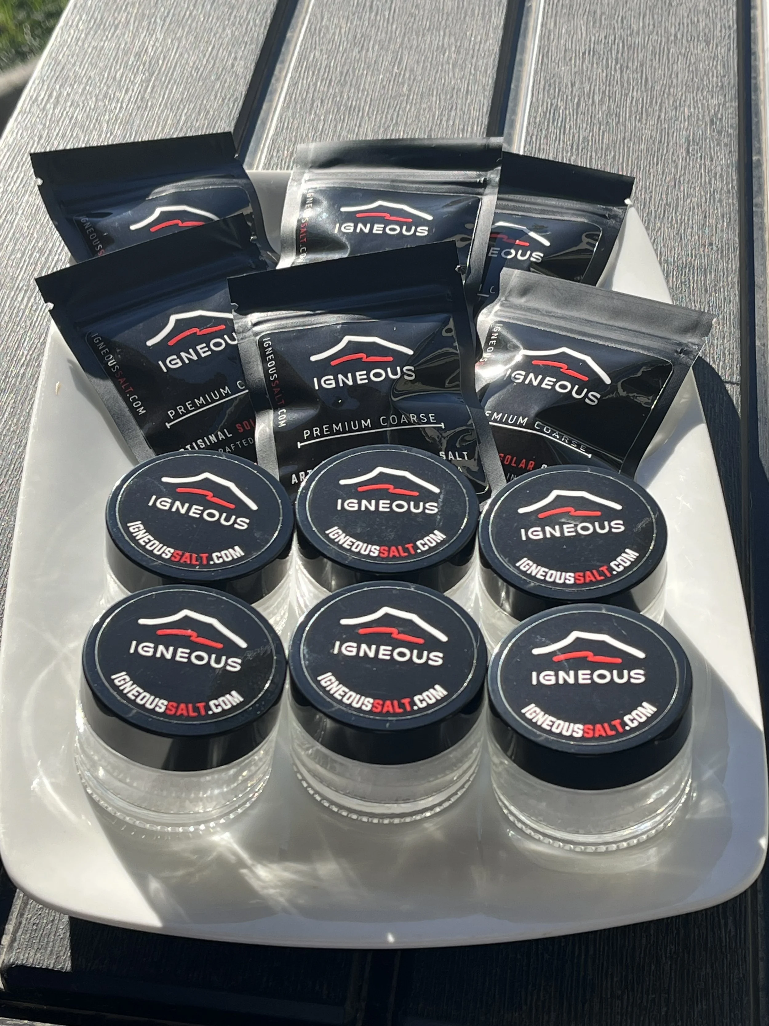 Assorted Ign&eacute;ous salt containers on a white tray outdoors, including small jars and packets of premium coarse and solar salt.