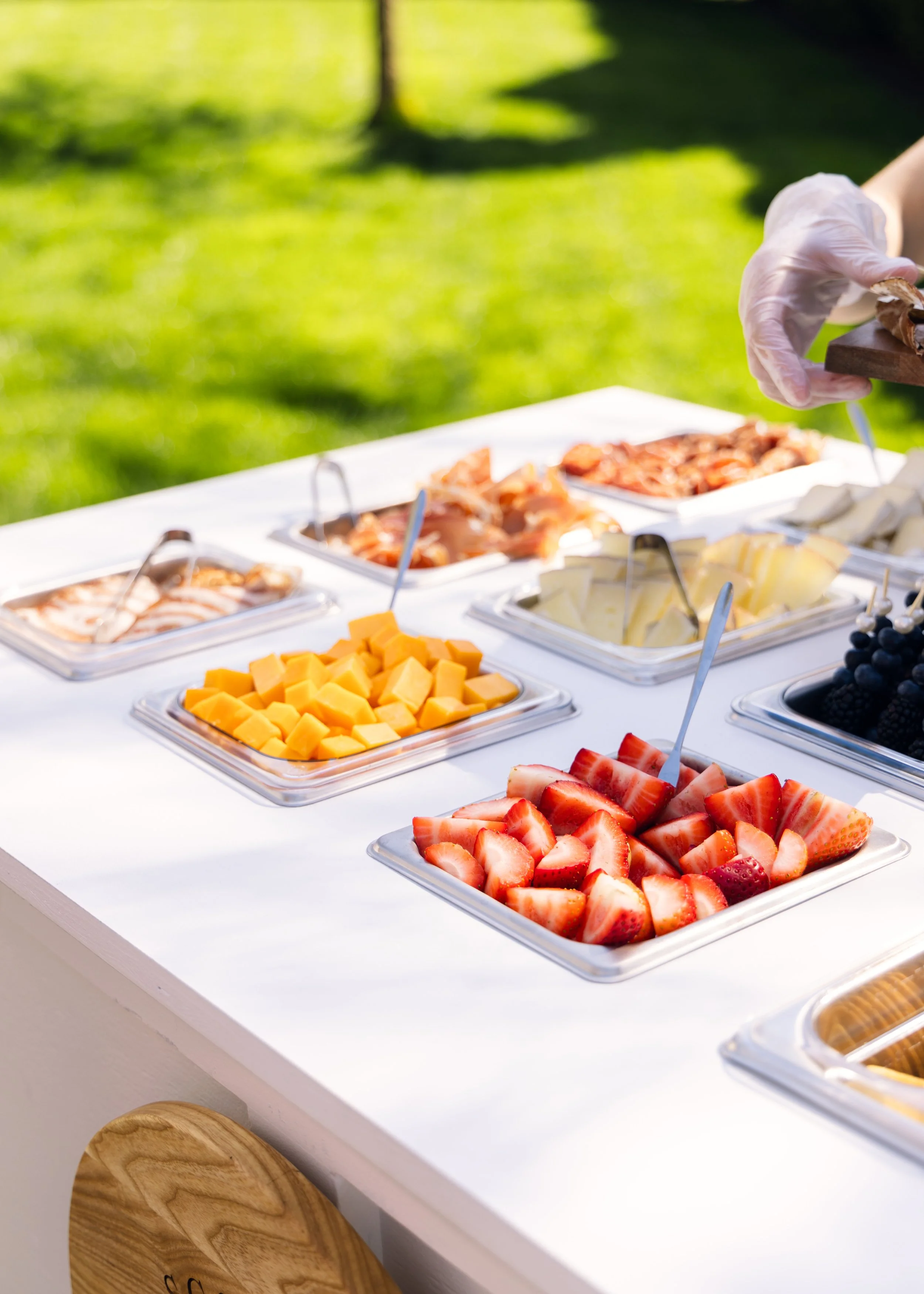An outdoor charcuterie cart with trays of sliced strawberries, cheese cubes, and beautifully assorted appetizers. 