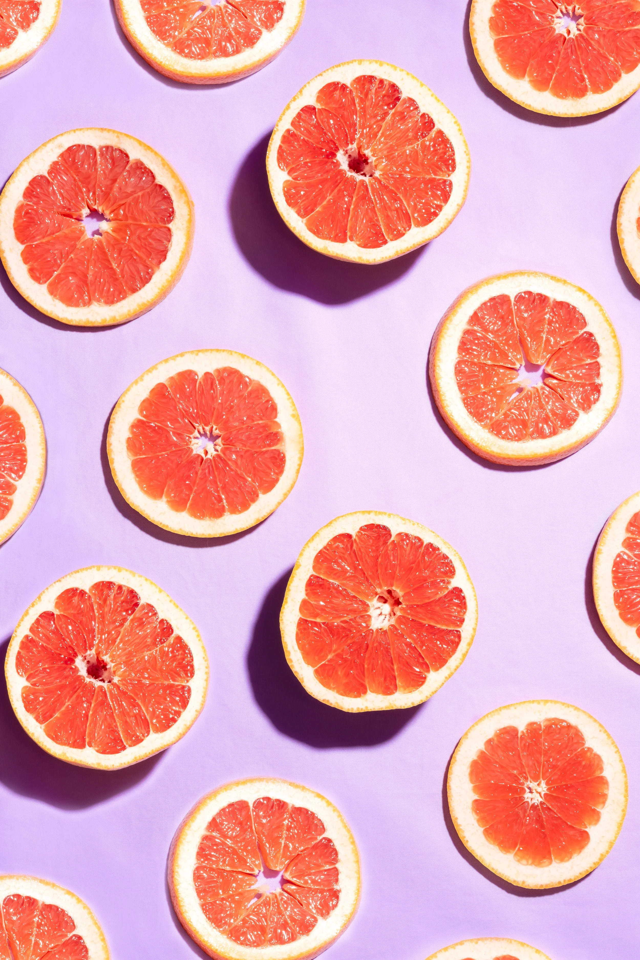 Multiple halved grapefruits on a purple background.