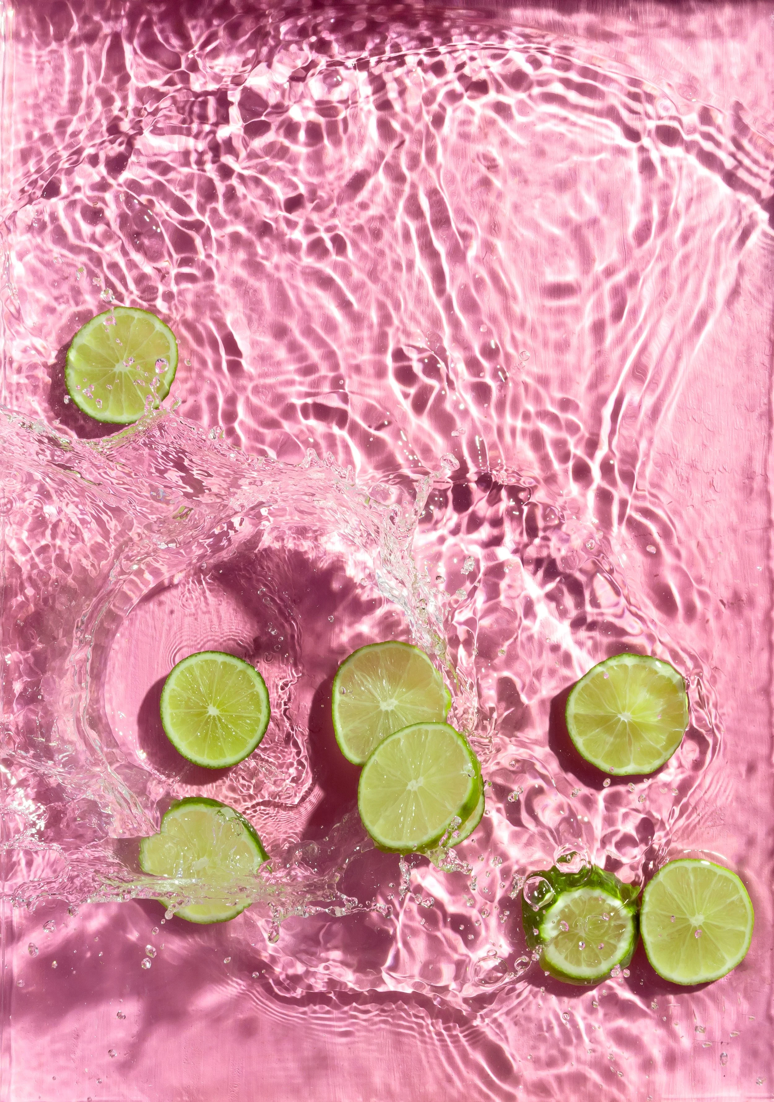 Lime slices floating on pink water with ripples and splashes.