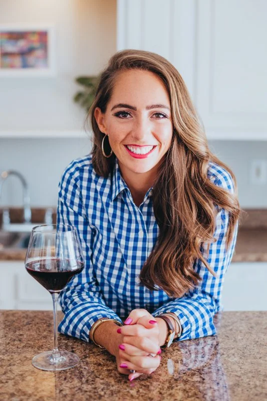 a woman leaning against a kitchen counter with a glass of wine next to her
