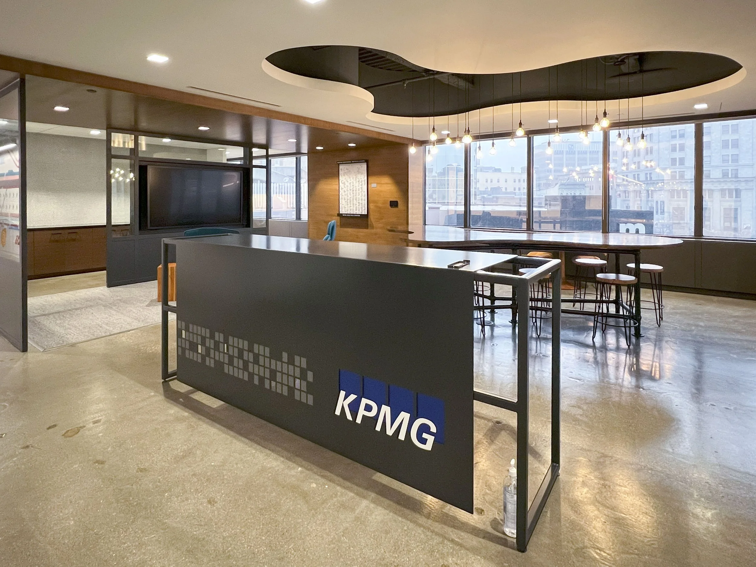 Interior of a modern office lobby with large windows, hanging lights, a reception desk with a KPMG sign, and a cityscape view outside.