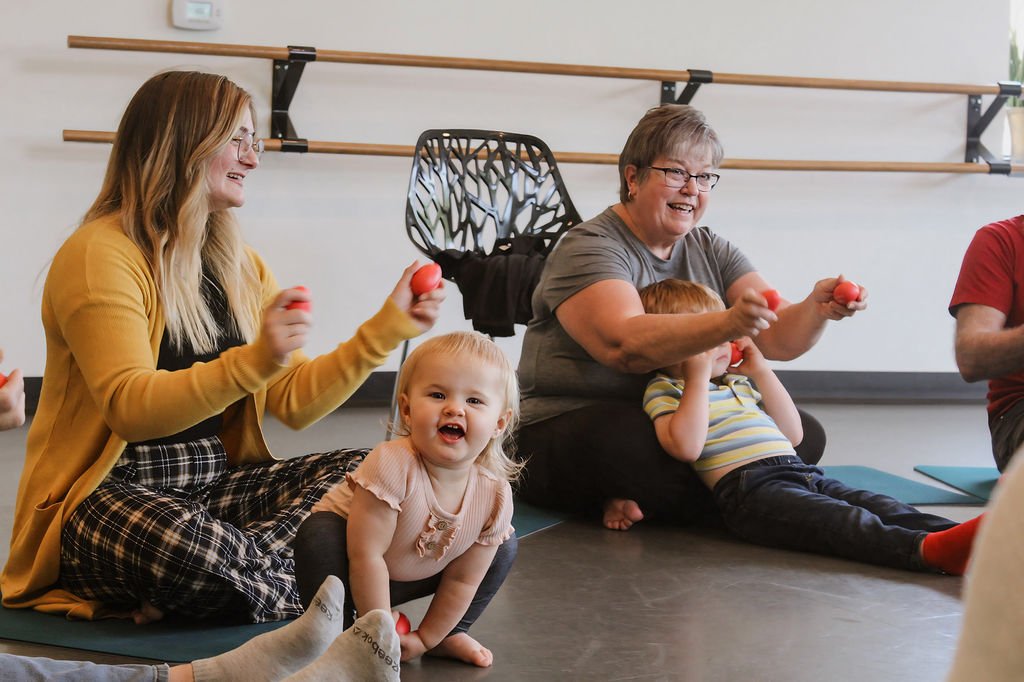 toddler smiling and families singing and playing egg shakers in music class
