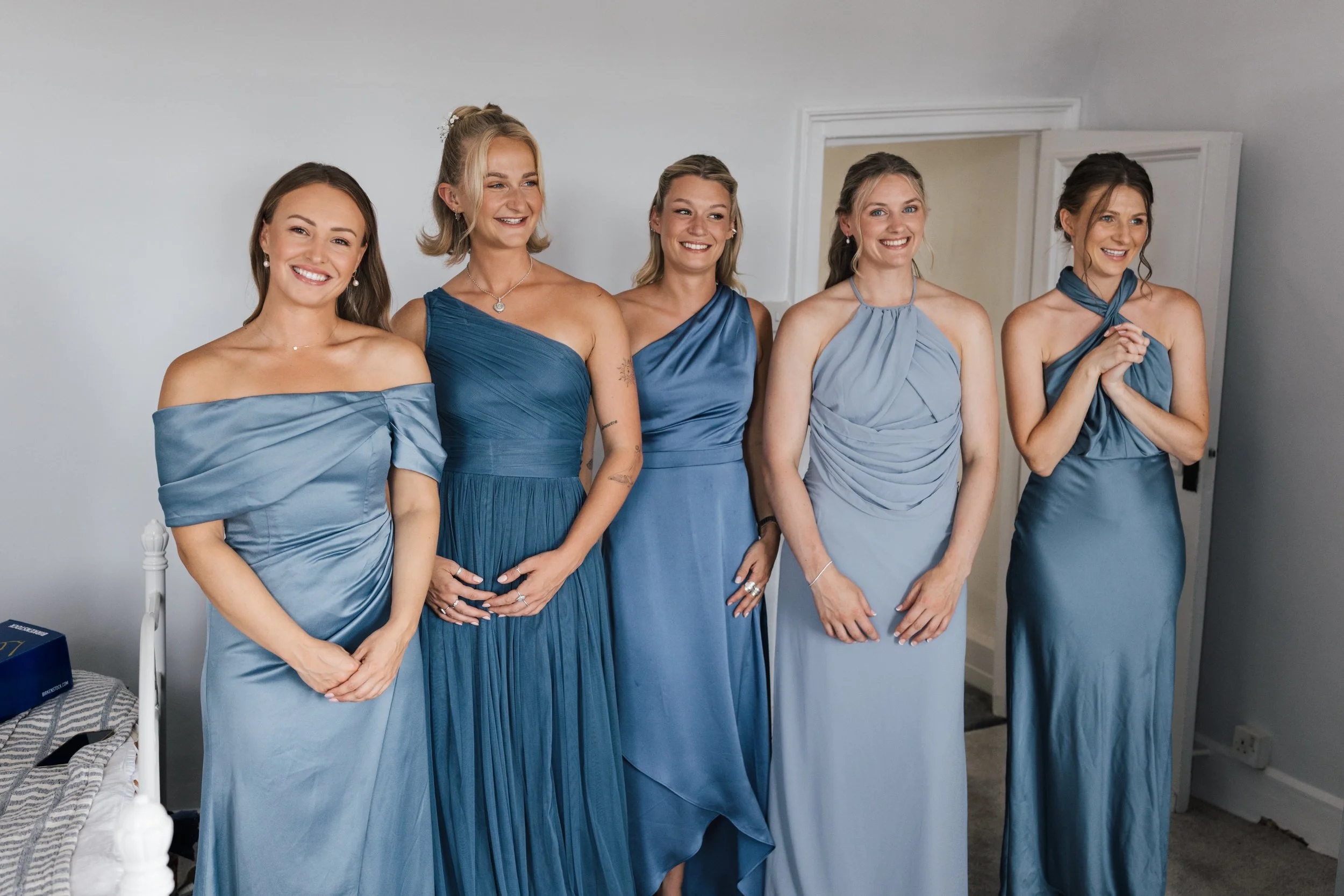 Five women dressed in matching blue dresses, standing side by side indoors, smiling.