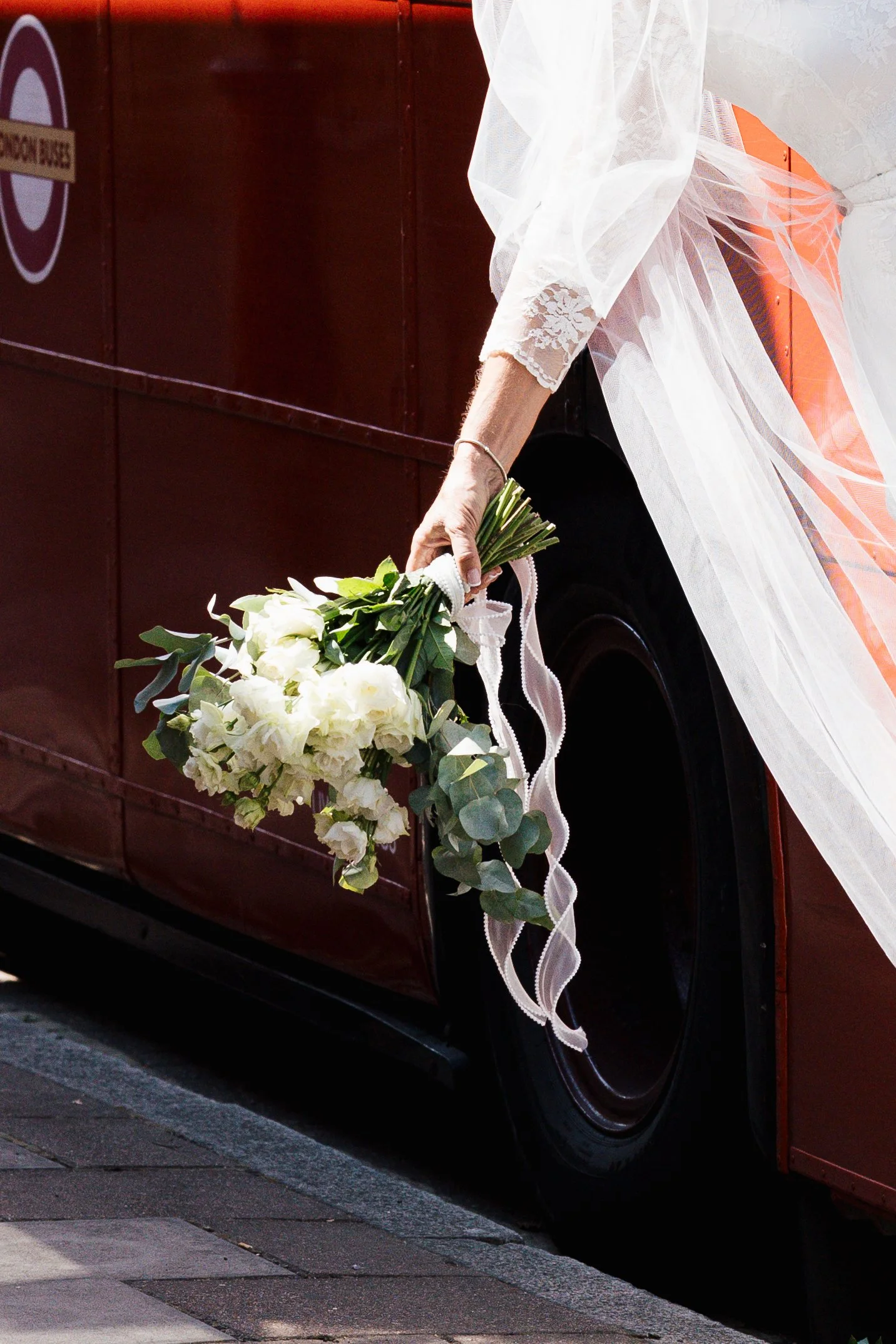 Close-up of a vintage car decorated with white flowers, lace, and ribbons for a wedding, parked on a city street.