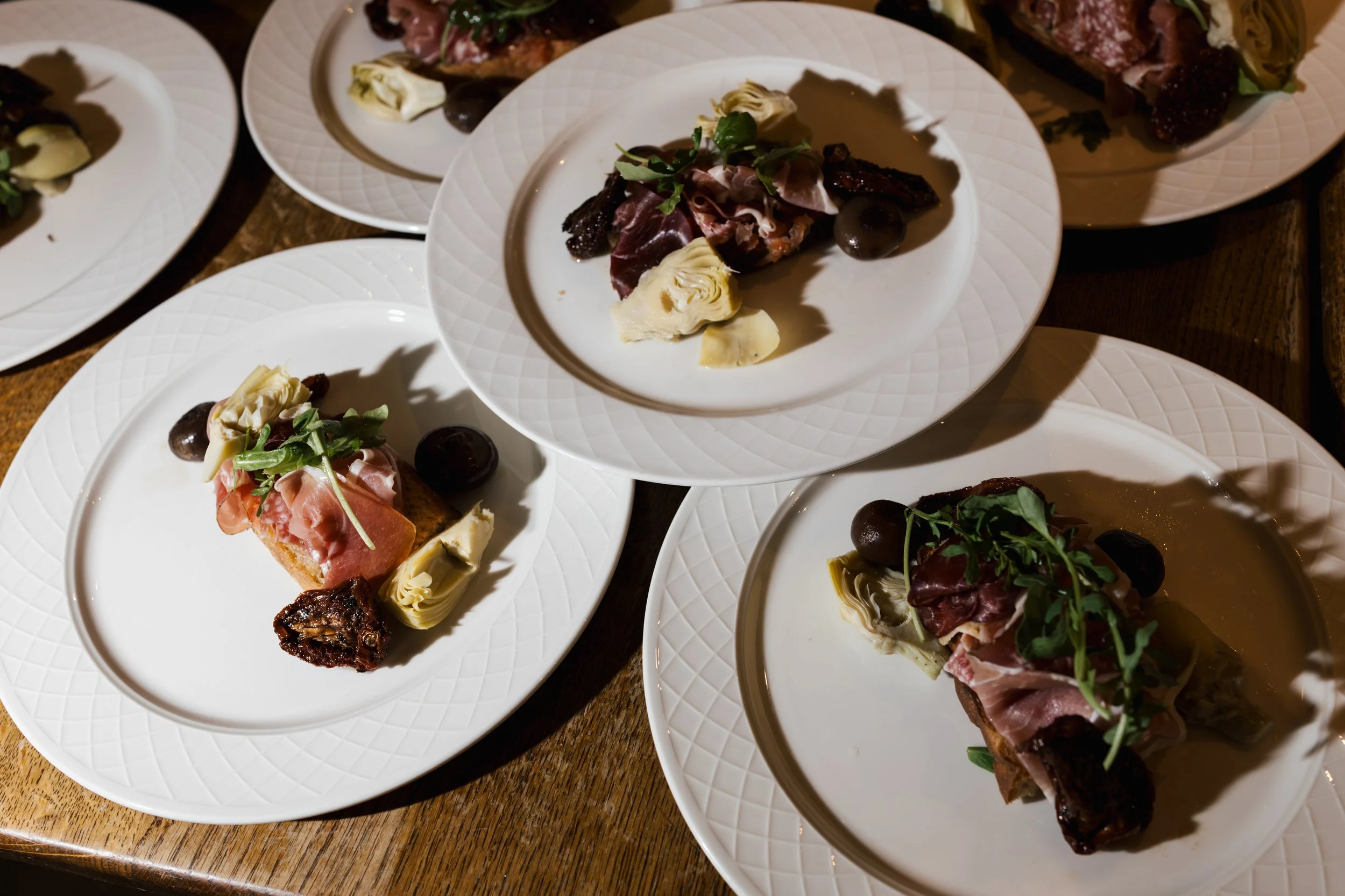 Multiple white plates with assorted appetizers and small portions of food on a wooden table.
