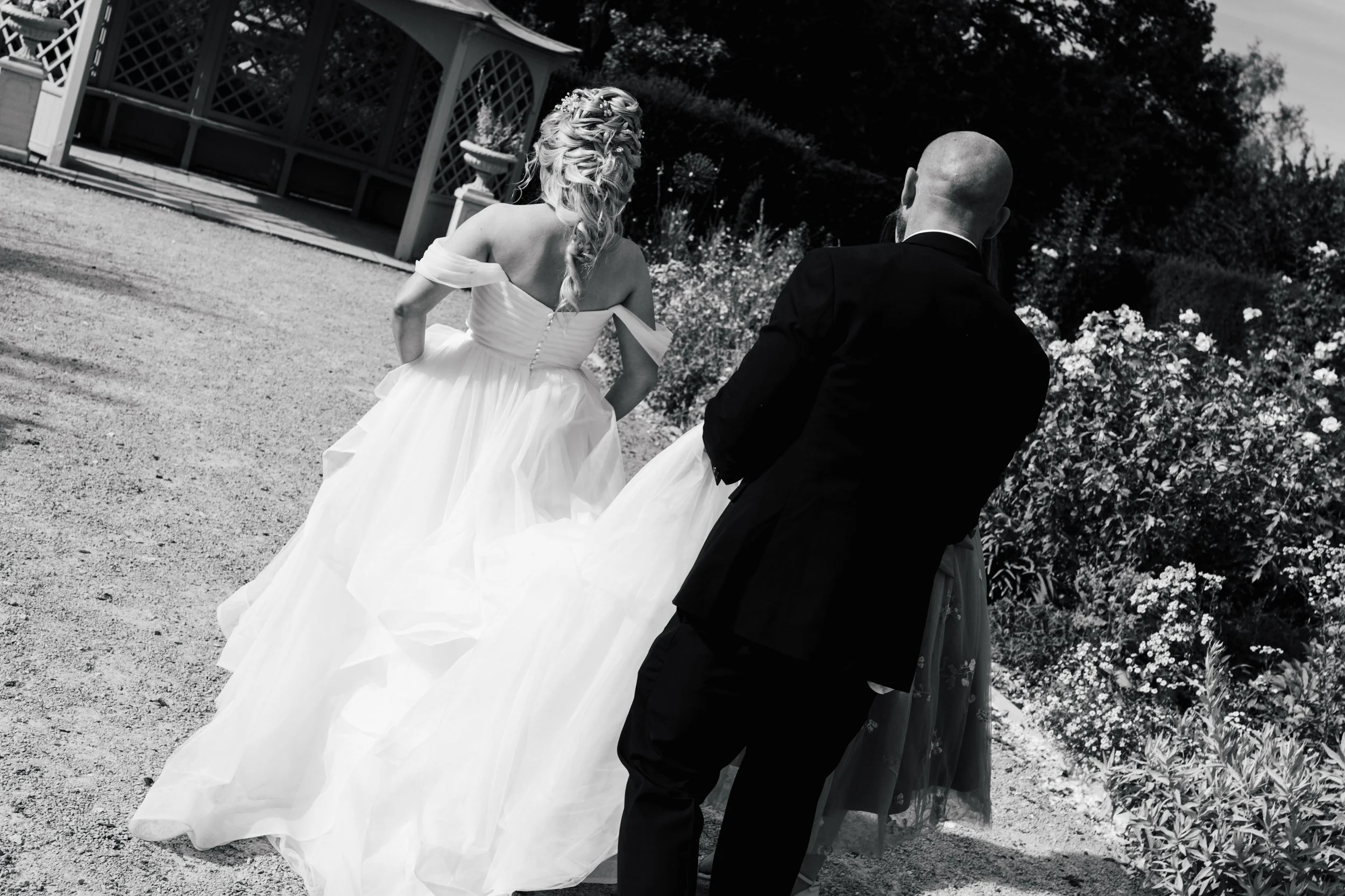 A bride in a wedding dress and a groom in a suit standing outdoors near a garden