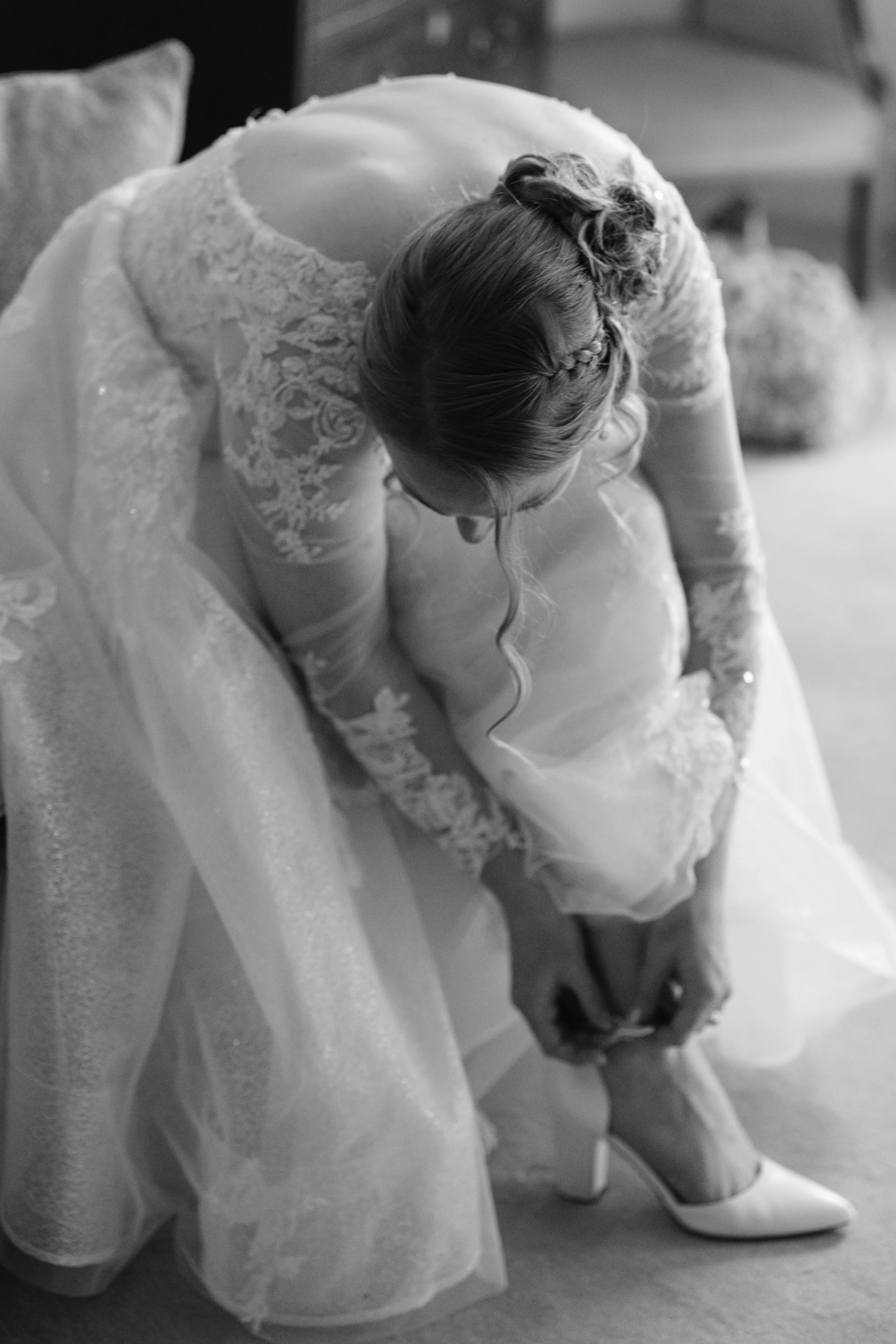 A woman in a wedding dress is bent down, putting on her shoe.