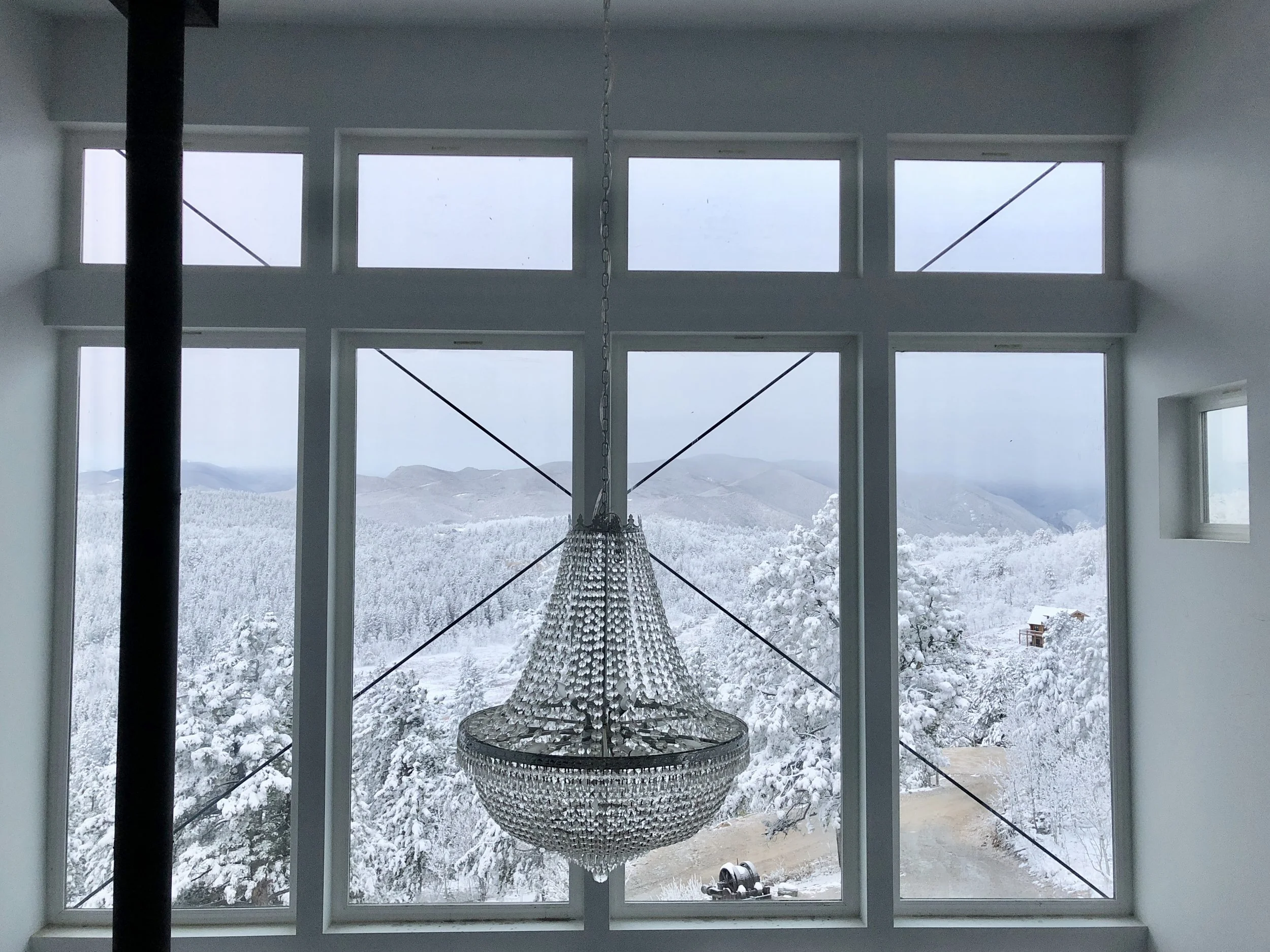Crystal chandelier hanging in front of large windows overlooking snow-covered mountain forest and hills