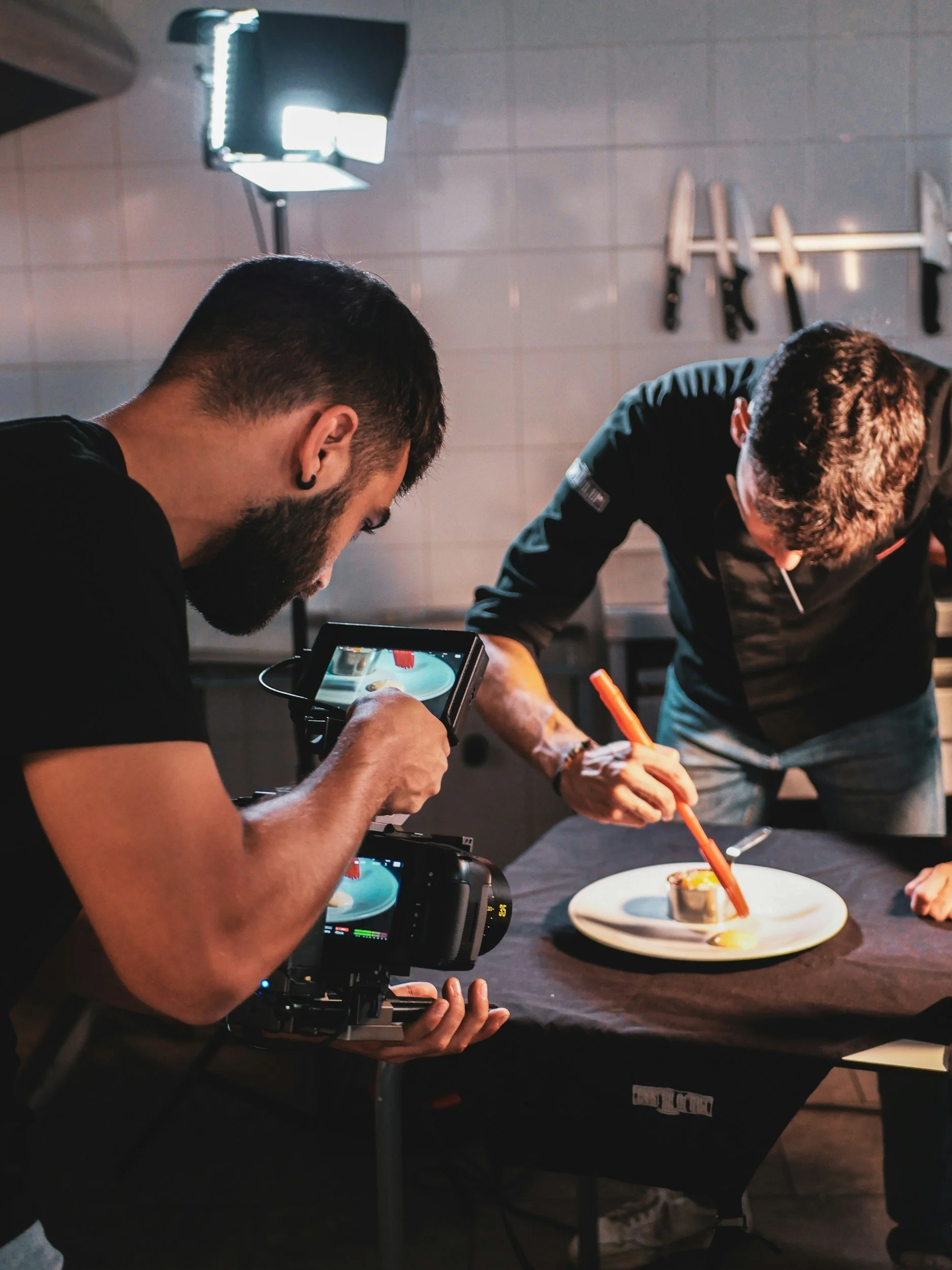 Videographer filming a chef plating a dish in a restaurant kitchen