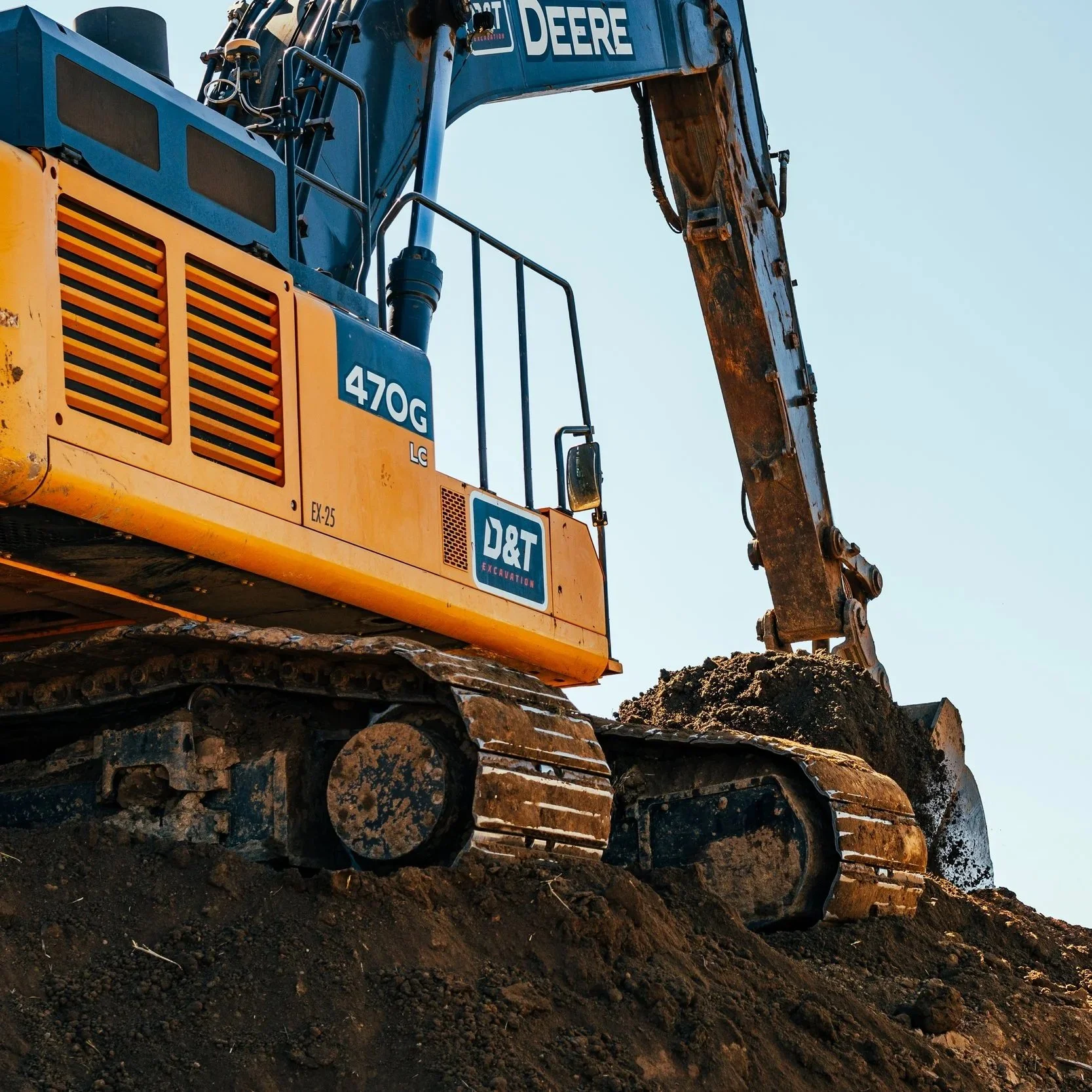 A John Deer 470G excavator with tracks on dirt, labeled with 'D&T Excavation', digging and moving earth in Portland, OR.