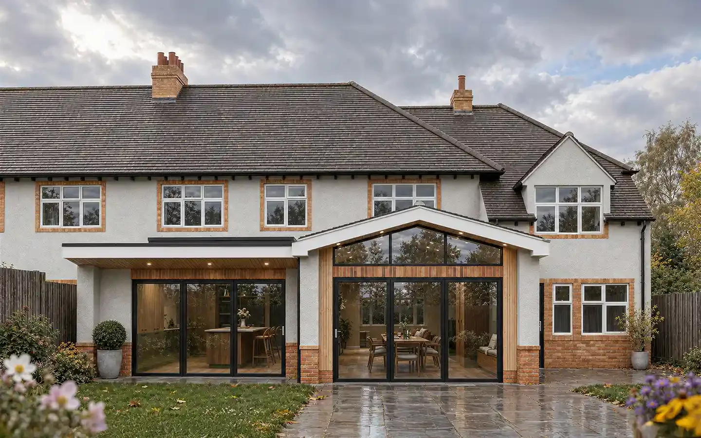 Garden view of a single-storey kitchen and dining extension in Stratford-upon-Avon, with black-framed bifold doors, a glazed gable and adjoining flat roof.