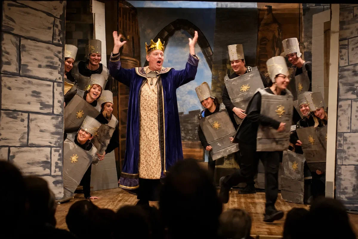 King Duncan in a regal costume frustrated with his guards at the castle