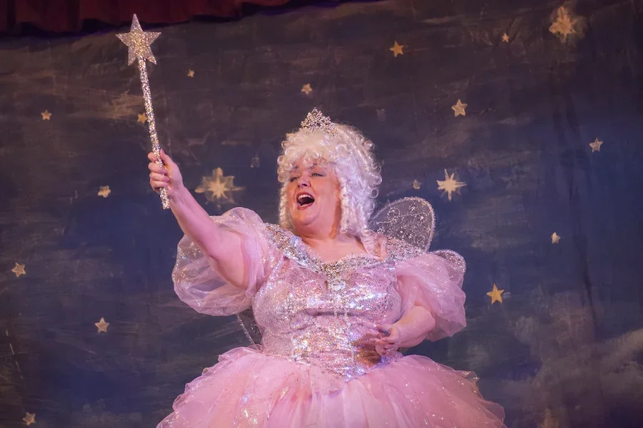 A panto fairy in a bright pink costume waving her magical wand