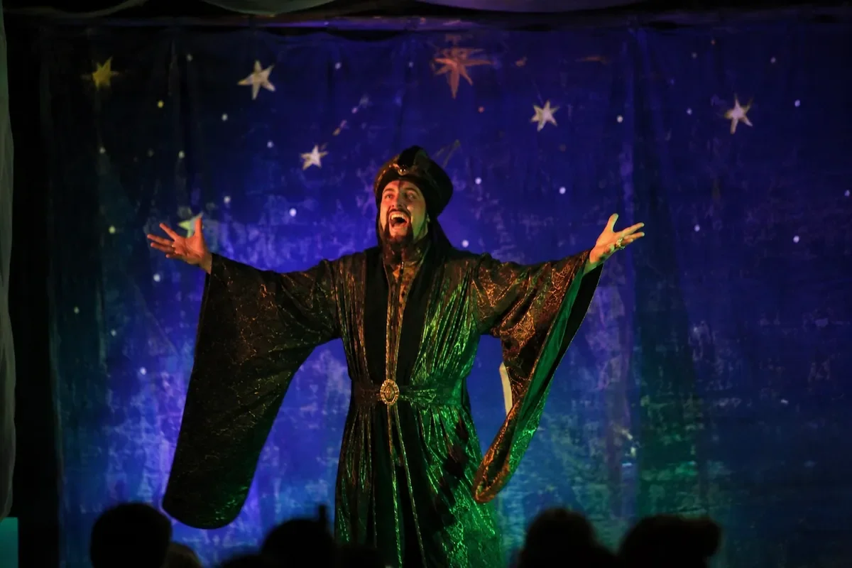 Abanazar in a black and gold cloak talking to the Audience