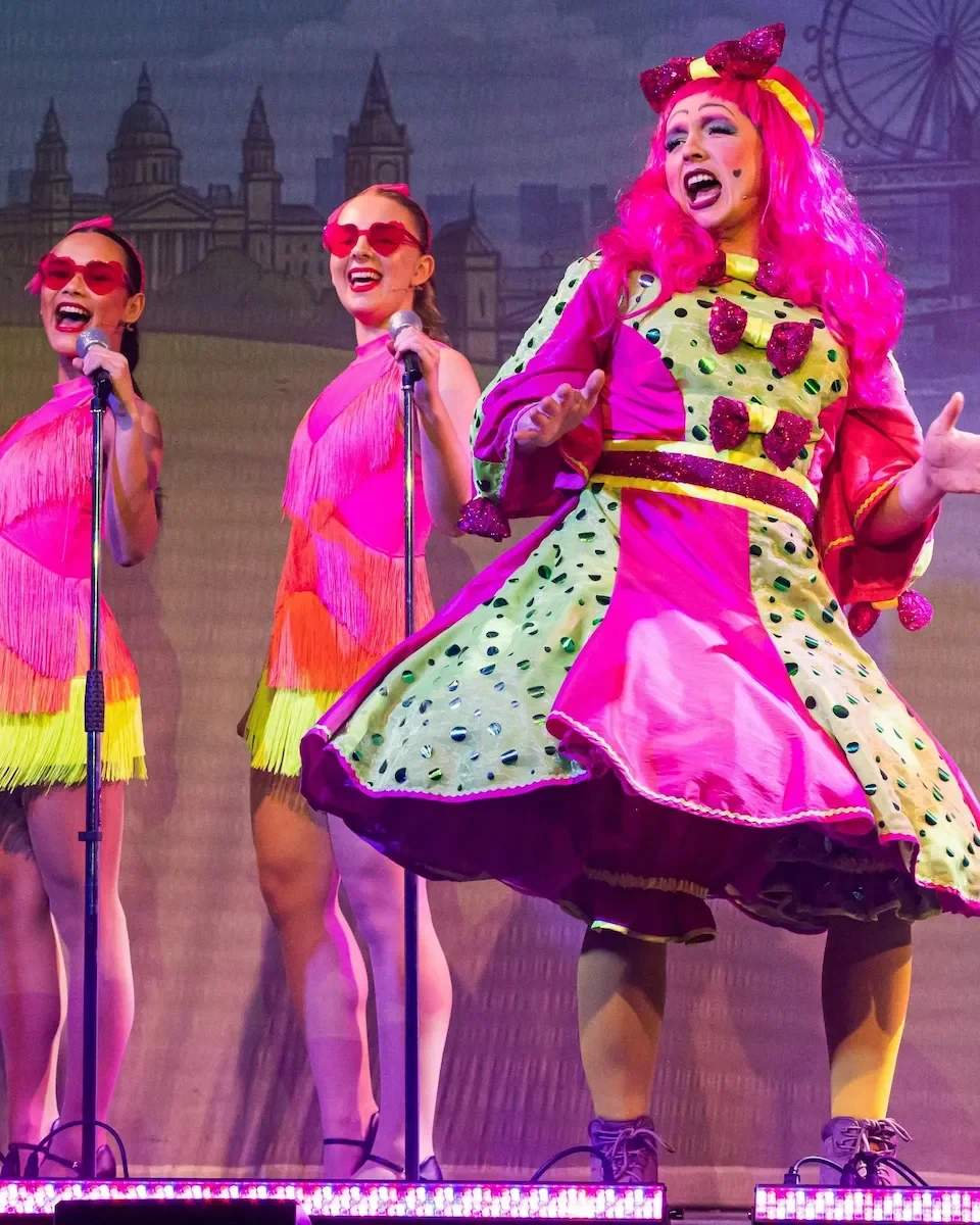 Performers in bright pink costumes singing in a pantomime performance