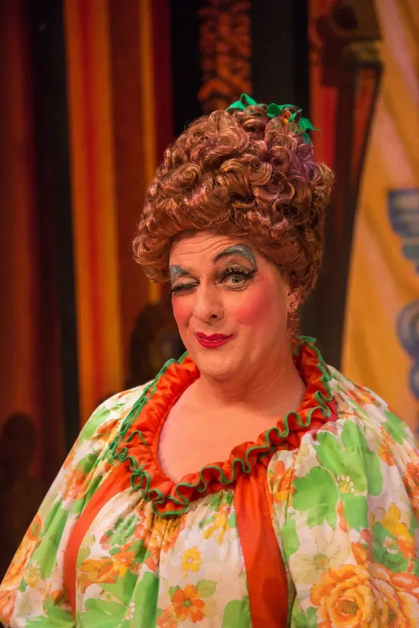 A pantomime dame winking at the audience in a production of Alice in Wonderland