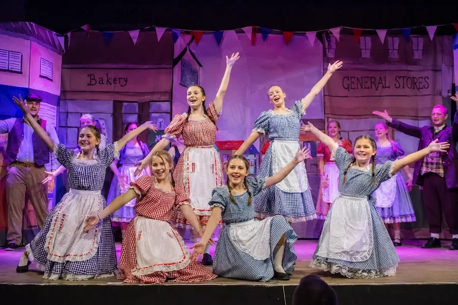 Ensemble singing and dancing in matching gingham costumes