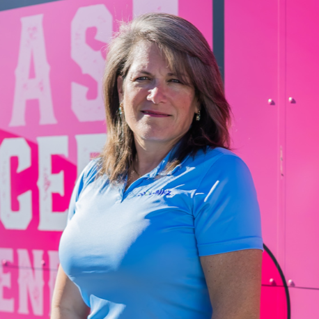 A smiling woman with glasses, brown hair, and a black jacket sitting on stairs.