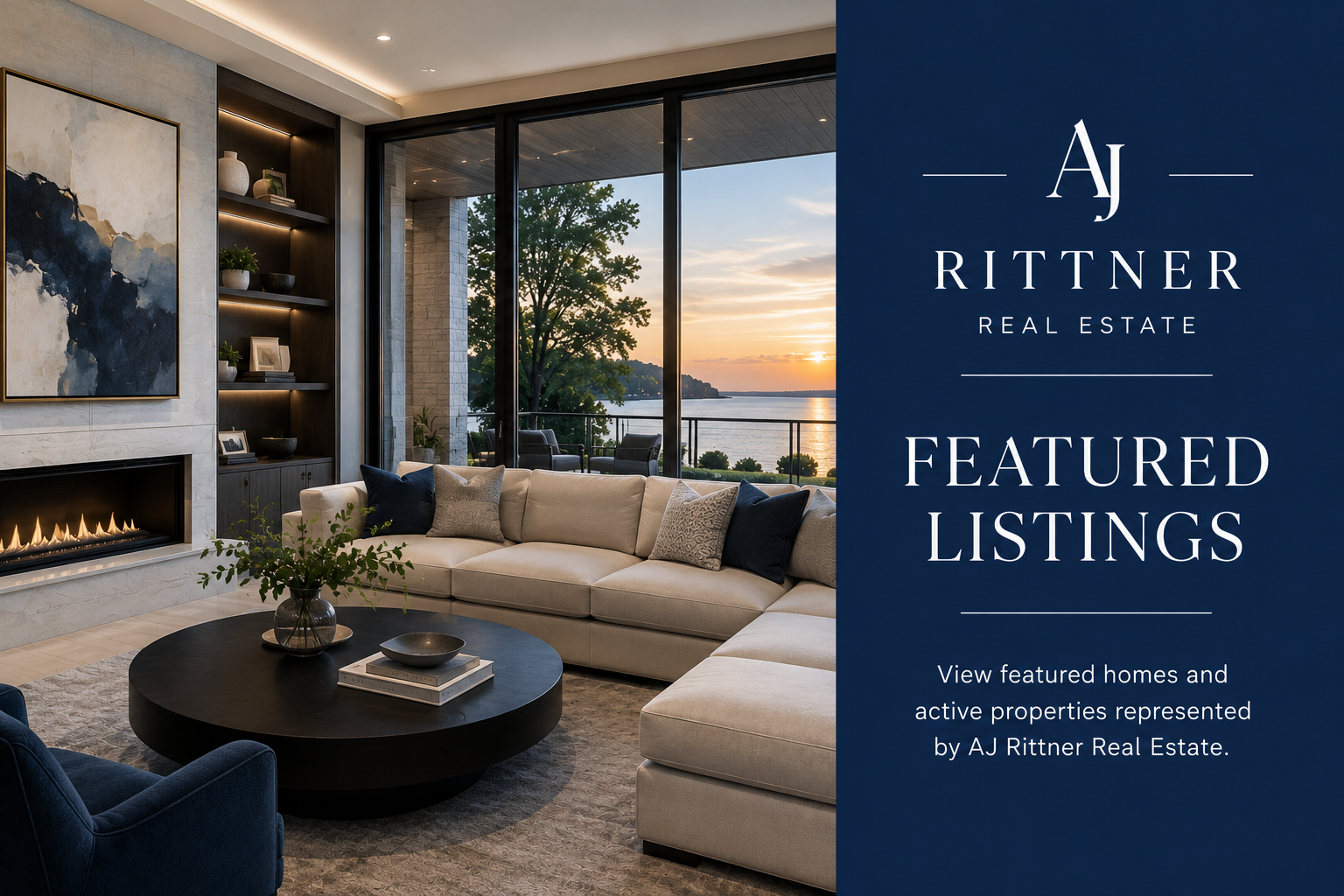 Interior view of a modern living room with a large beige sectional sofa, a round black coffee table, and a fireplace with a blue and white abstract painting above it. Large floor-to-ceiling windows reveal a sunset over a river and trees outside.