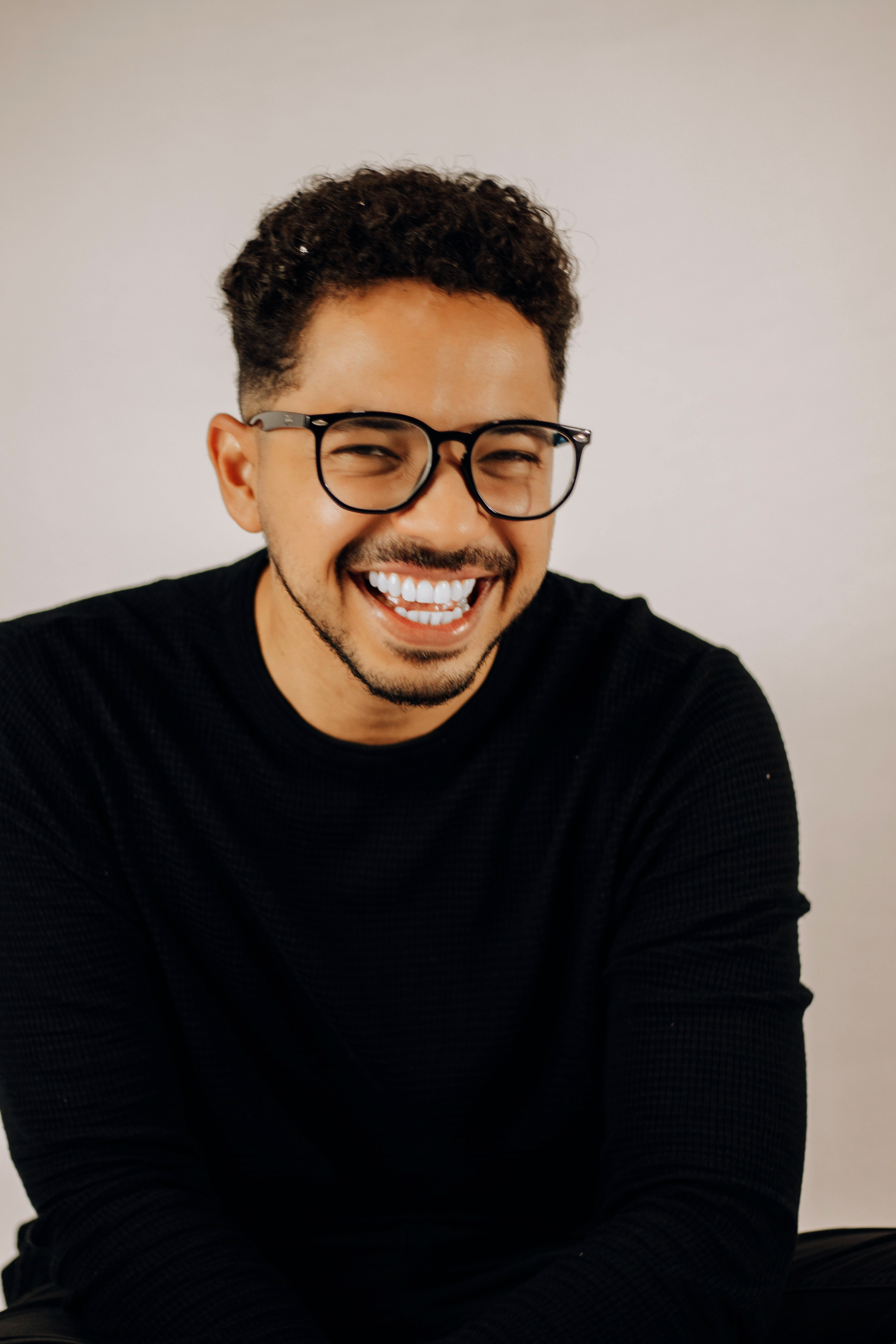 counselling Kitchener. A smiling man with curly hair and glasses, wearing a black sweater, sitting against a plain light background.