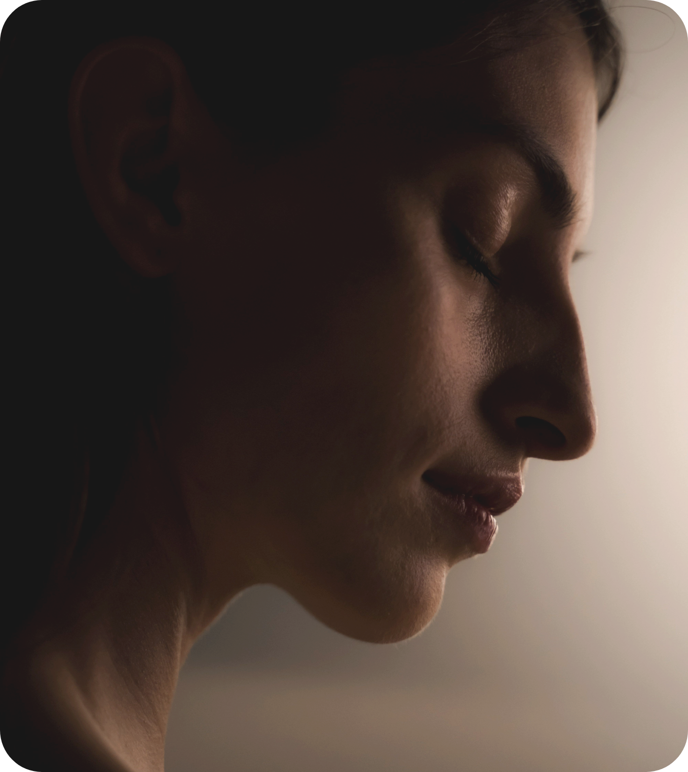 Close-up of a woman with her eyes closed, side profile, with dramatic lighting highlighting her facial features and smooth skin.